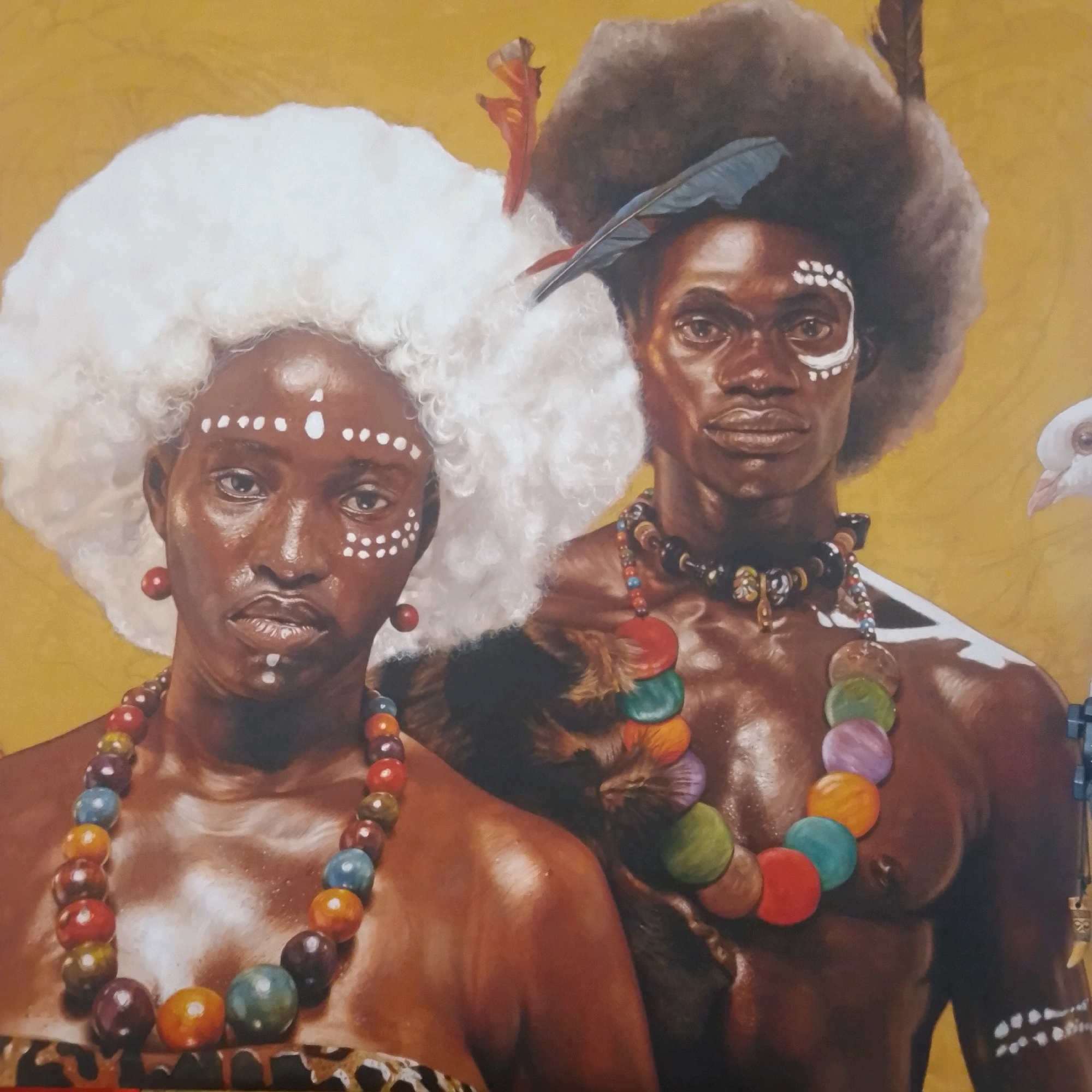 This is a detailed, realistic oil painting featuring two individuals, likely a man and a woman, adorned with traditional markings and jewelry. The background is a textured yellow, reminiscent of a wall or canvas.
The woman on the left has a large, voluminous white afro and wears large red circular earrings. Her face is painted with white dots, forming a pattern above her eyes and on her forehead. She is wearing a necklace made of large, colorful beads in shades of red, orange, yellow, green, blue, and purple. A leopard-print fabric is visible around her shoulders.
The man on the right has a large, dark afro and wears a feather in his hair. His face also has white markings, including a curved line above his eye and dots on his cheekbone. He is wearing a dark necklace with smaller, multi-colored beads and a larger pendant. A white bird, possibly a dove, is visible in the upper right quadrant of the painting. The man's chest and shoulders are bare, showcasing his skin tone and muscle definition, which are highlighted by what appears to be oil or sweat.
The painting is rendered with a high degree of skill, capturing lifelike textures and colors. The subjects are depicted with direct, serious gazes. The overall impression is one of cultural representation and artistic portrayal of individuals in traditional attire. There is no information in the image itself to suggest a specific location in Ado, Nigeria.
