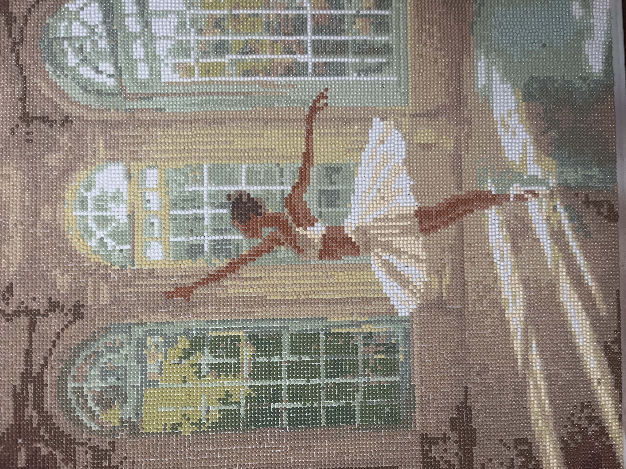 A diamond painting depicts a ballerina leaping through a room with three windows. The windows are rectangular with rounded tops and divided into small panes. Outside, the view is predominantly green, possibly foliage. The dancer is mid-air, her arms outstretched, and wearing a white tutu. Light streams into the room from the right, casting shadows. The room's decor is in earth tones. The location is Unknown, Unknown.