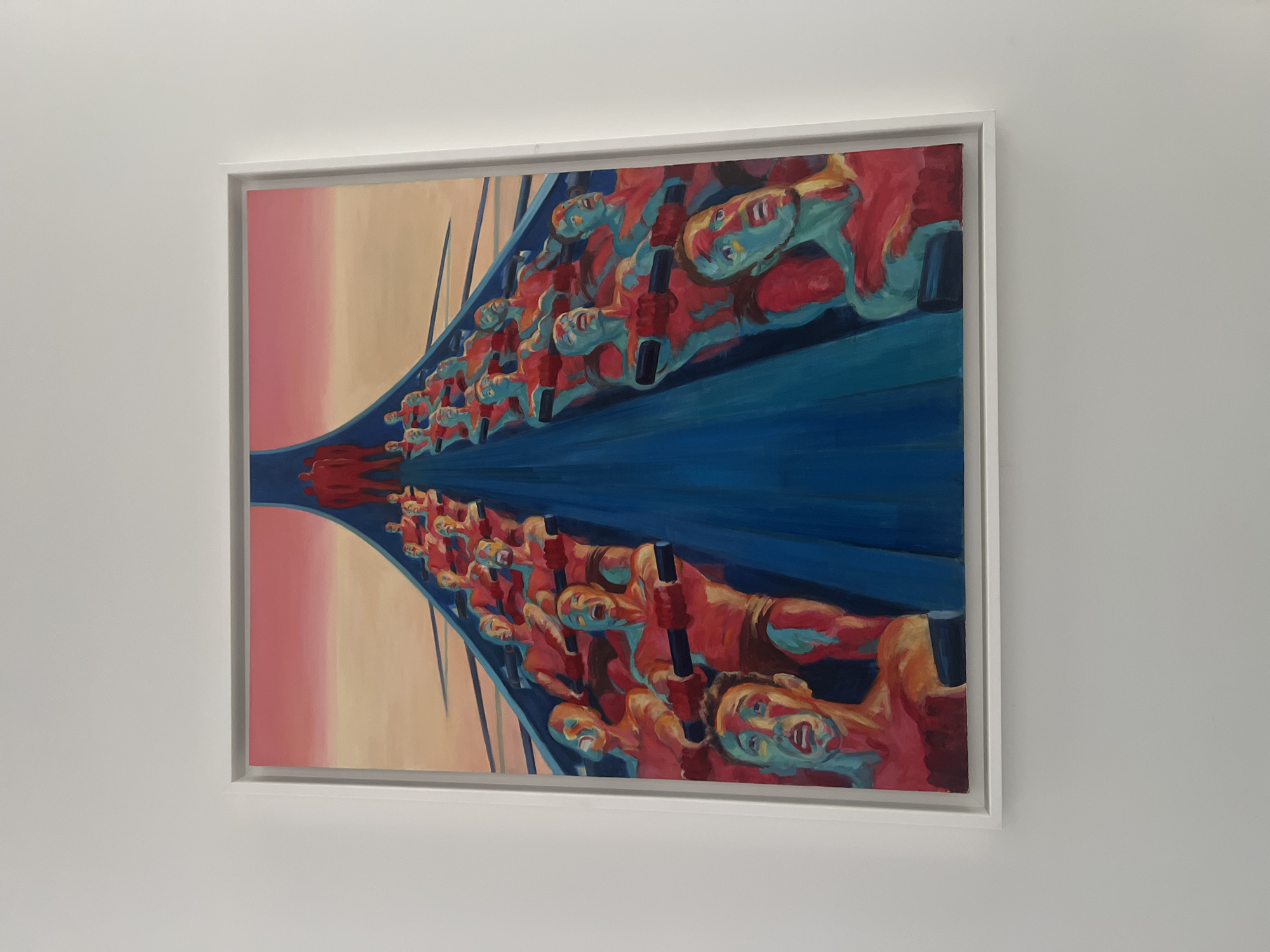 A framed painting hangs on a white wall. The artwork depicts two rows of people rowing a boat. The background is a gradient of pink and beige. The boat and water are blue. The rowers are painted in shades of red and blue. The painting is likely located in Saint Petersburg, Russia due to the style of the artwork and the presence of rowers, a common theme in art from that region.