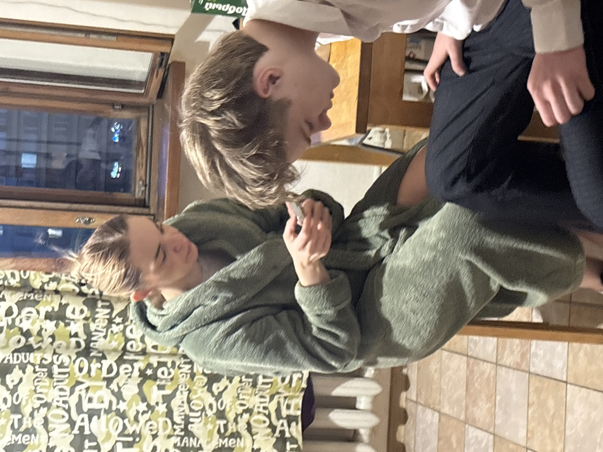 Two individuals are present. One is wearing a white shirt and dark pants, while the other is wearing a green hooded jumpsuit. The latter is holding an object in their hand. They are indoors. The location is Unknown, Unknown.