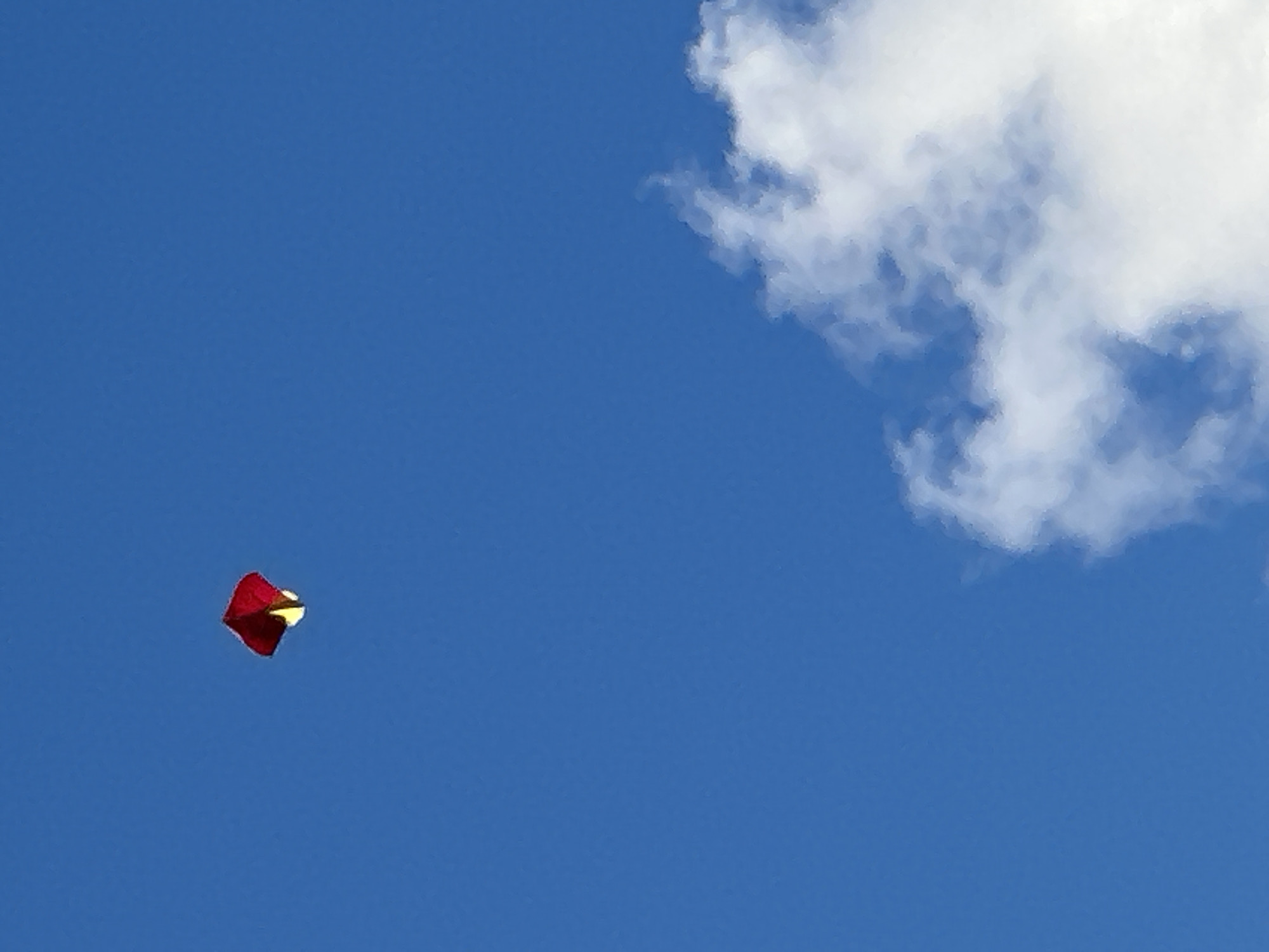A red and yellow kite is flying in a clear blue sky. There is a white cloud in the lower right quadrant of the image.