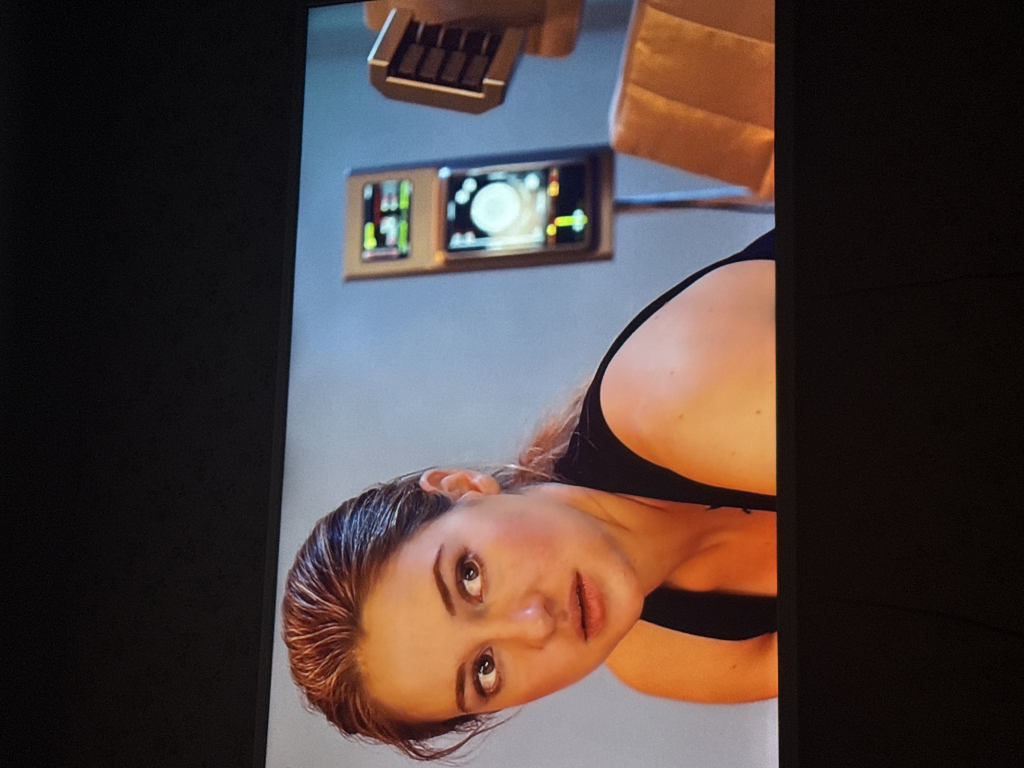The image depicts a woman with wet hair looking upwards. She is wearing a black tank top. Above her are controls and instruments mounted on a structure. The background appears to be a gray or light blue wall. The location in Mytishchi, Russia, cannot be determined from the image alone.