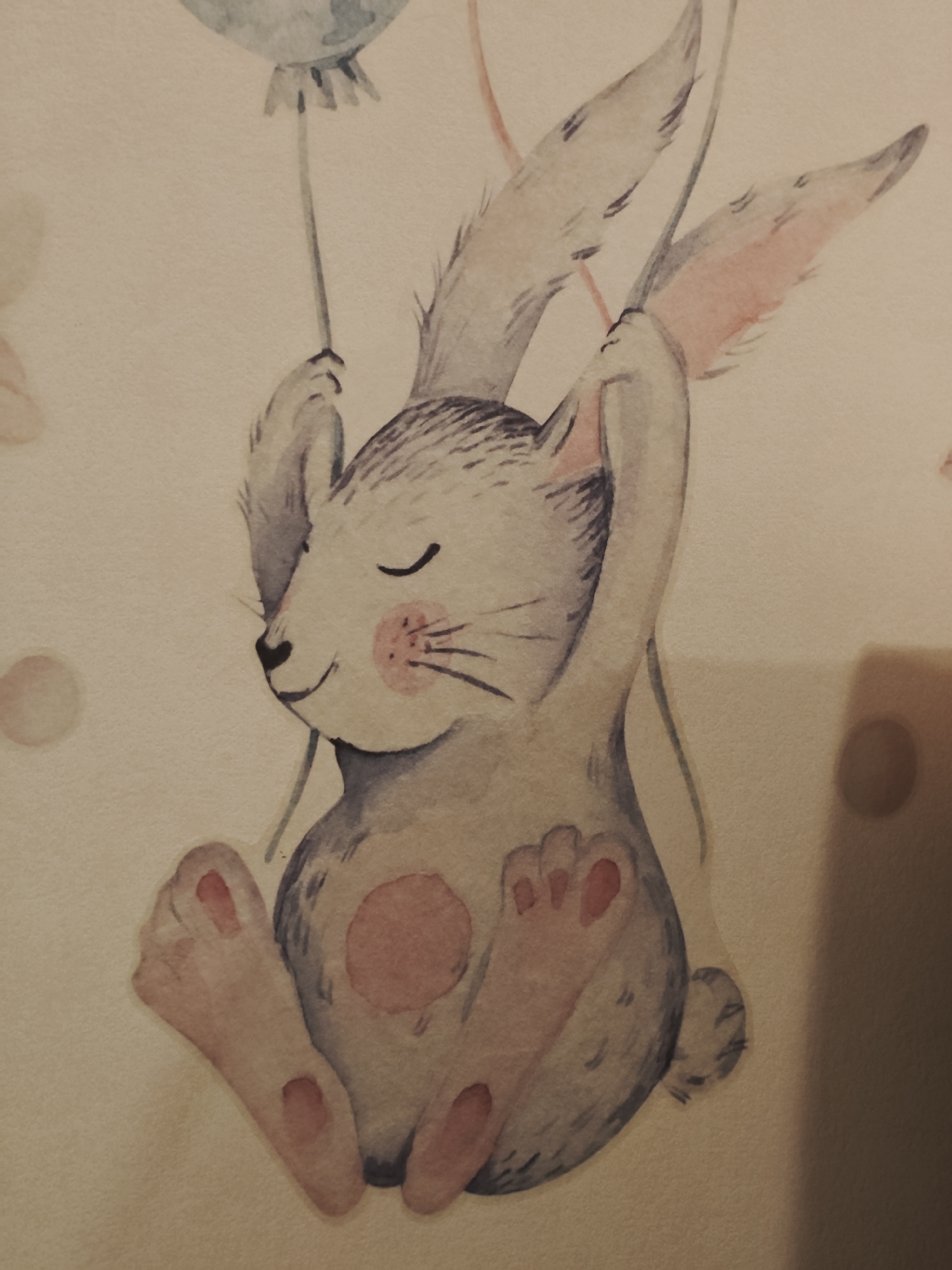 A watercolor illustration depicts a whimsical bunny character holding onto a balloon string. The bunny is rendered in shades of gray and pink, with closed eyes and a gentle smile. Its ears are long and prominent, and its paws are detailed with pink pads. The background is a soft, neutral tone with a few subtle, circular elements. The image is a piece of art, not a photograph of a specific location in Saint Petersburg, Russia.
