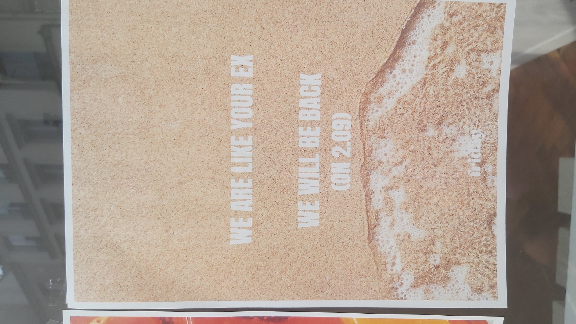 A poster with a sand and wave background is displayed. The poster contains white text that reads: "WE ARE LIKE YOUR EX WE WILL BE BACK (ON 2.09)". The poster is positioned in a window with a reflection of a building facade in the background, suggesting an urban setting. A portion of another poster with orange and yellow elements is visible to the left. The poster is located at 24 Rue des Martyrs, 75009 Paris, France.