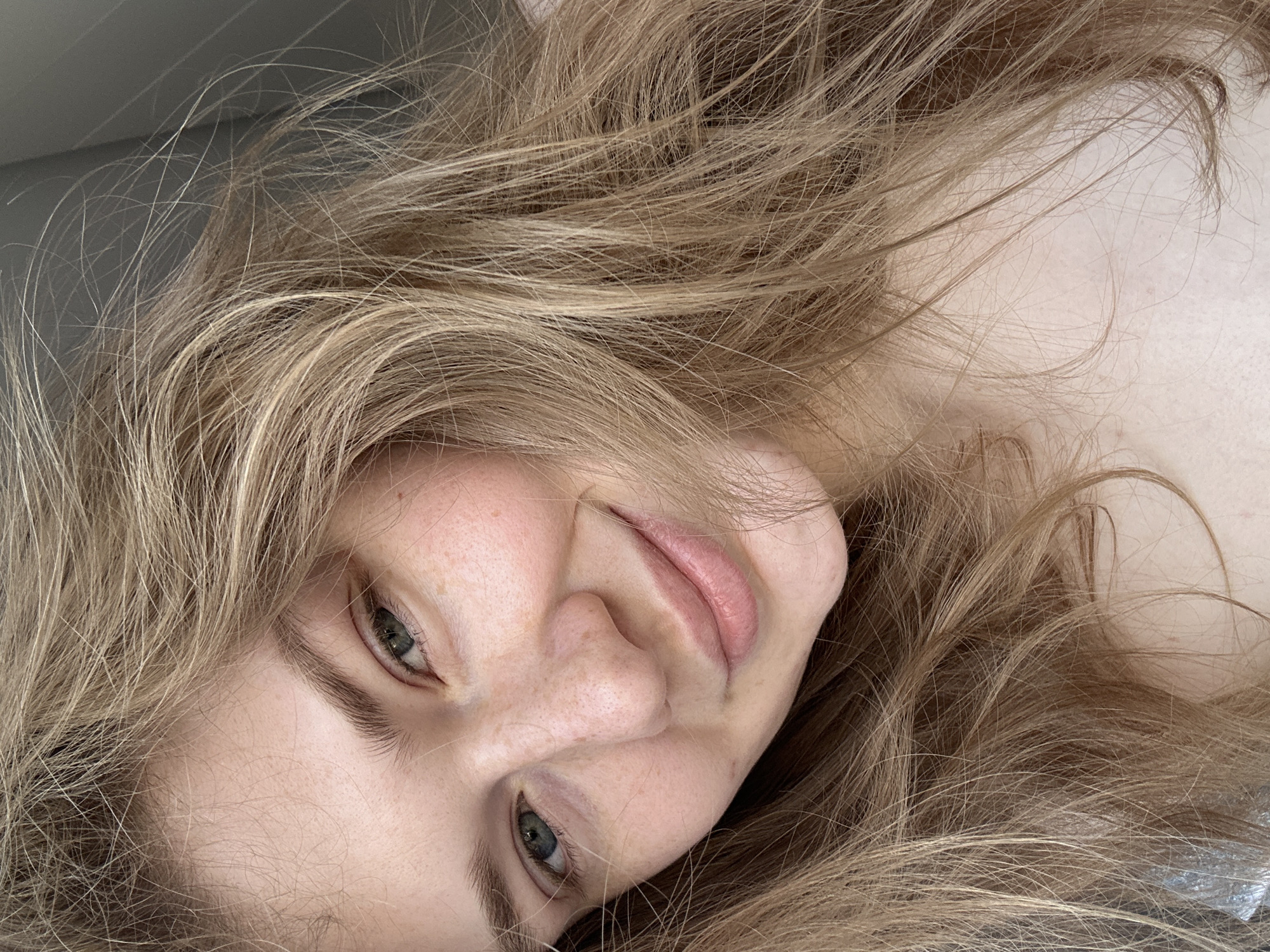 The image depicts a fair-skinned woman with long, blonde hair. Her eyes are green. The camera angle is close-up, slightly tilted. The background is out of focus. There is no indication the location is Kazan, Russia.