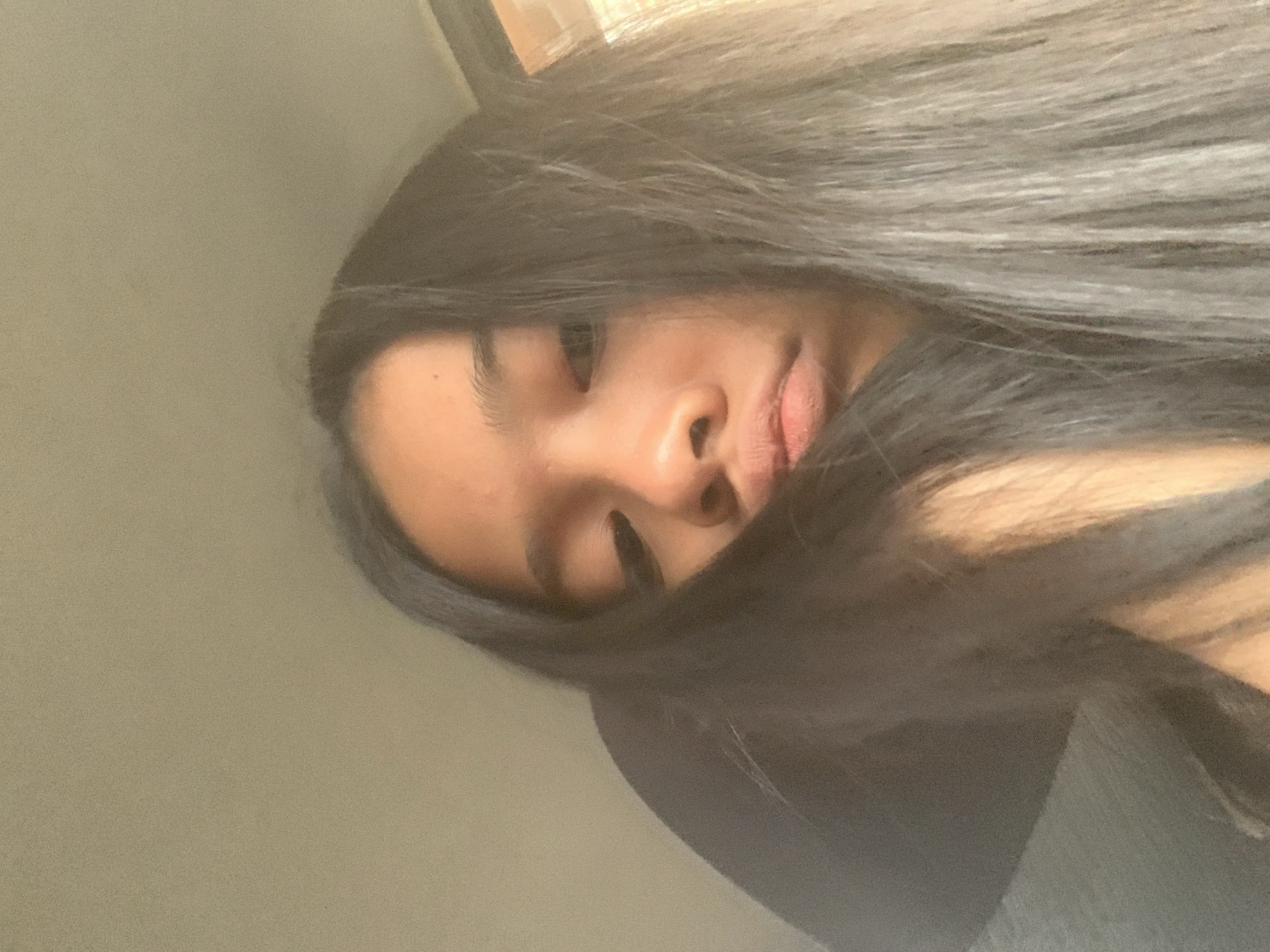 A close-up, angled shot of a person with long, dark hair partially obscuring their face. The individual's nose, lips, and one eye are visible. The background appears to be a light gray wall. The location, Samarinda, Indonesia, cannot be ascertained from the visual information.