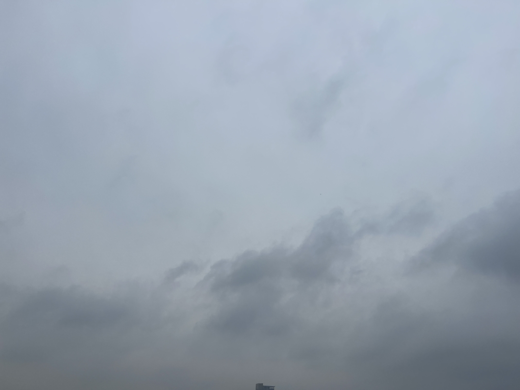 The image depicts a cloudy sky over the Jiangning District in China. The sky is filled with gray clouds, suggesting an overcast day. In the lower portion of the image, a building structure can be seen near the horizon line.