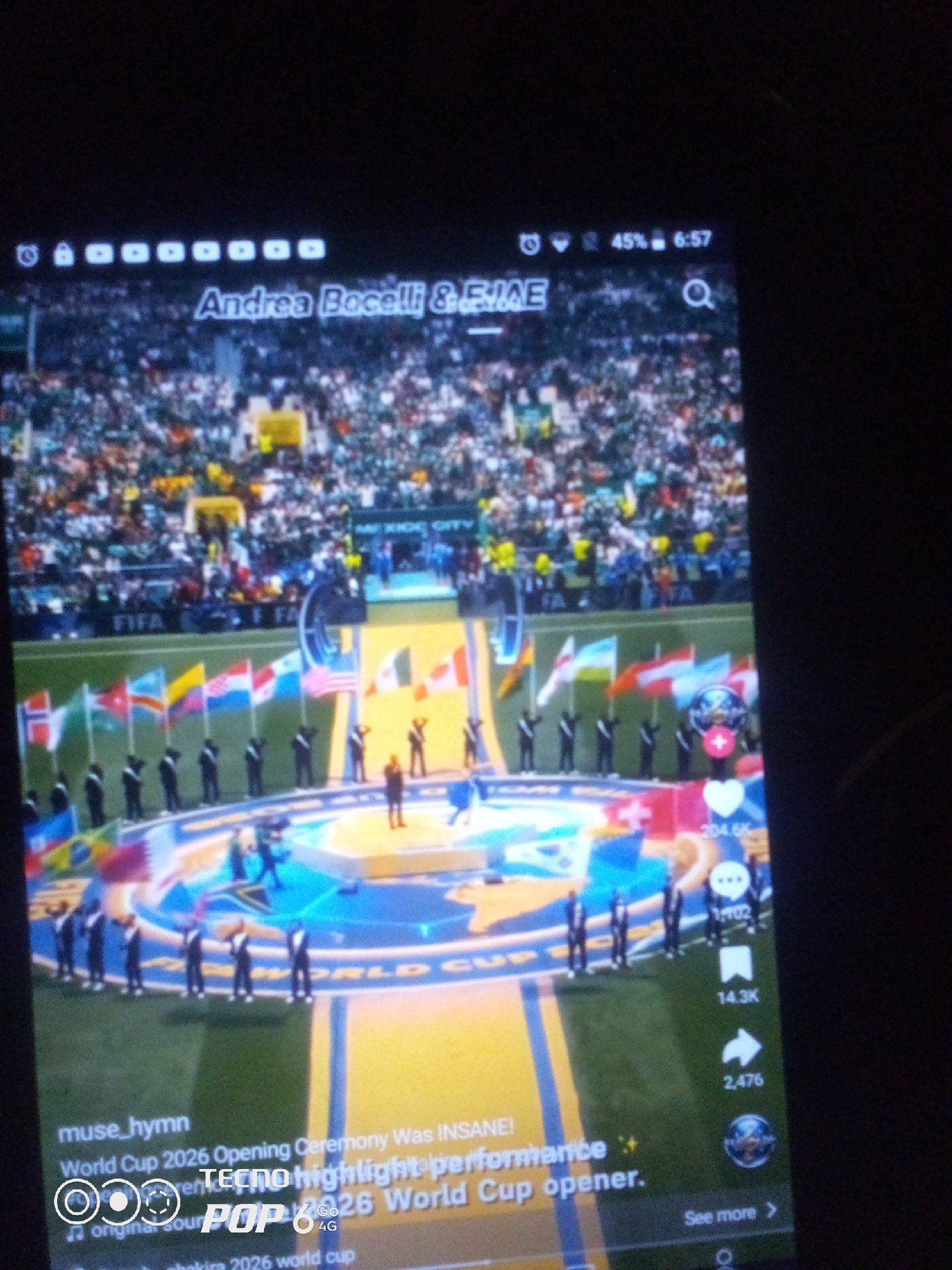 The image shows a screenshot of a mobile device displaying a video. The video appears to be a recording of the opening ceremony of the 2026 World Cup, featuring Andrea Bocelli and others. In the foreground, a stage with flags and performers is visible. The background shows a stadium filled with spectators. The mobile device's interface, including the time, battery status, and social media icons, is also partially visible. The location is not specified in the image, and there is no indication of Howayi, Nigeria.