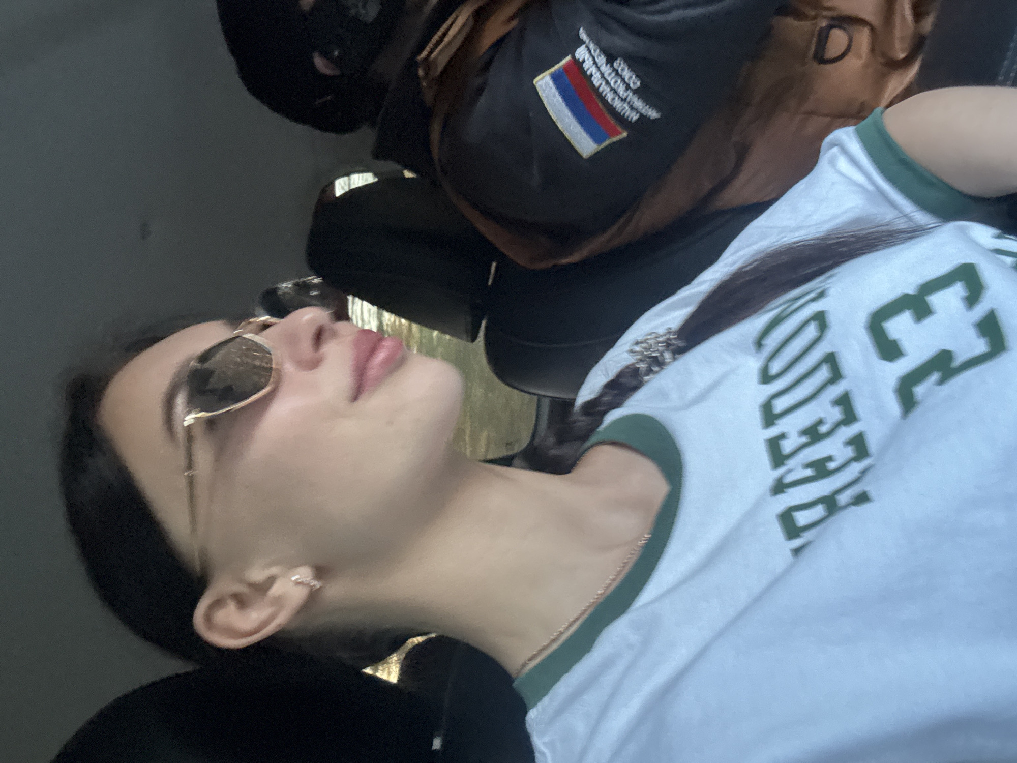 A selfie taken at an angle shows a young woman wearing sunglasses and a white T-shirt with green trim and "FREEDOM" printed on it. Beside her is a person wearing a black balaclava and a dark jacket with a Russian flag patch and the words "МУНИЦИПАЛЬНАЯ ПРОТИВОПОЖАРНАЯ ОХРАНА ГОРОДА ЧАЙКОВСКИЙ" (Municipal Fire Protection Chaikovsky City). The setting appears to be indoors, possibly inside a vehicle.