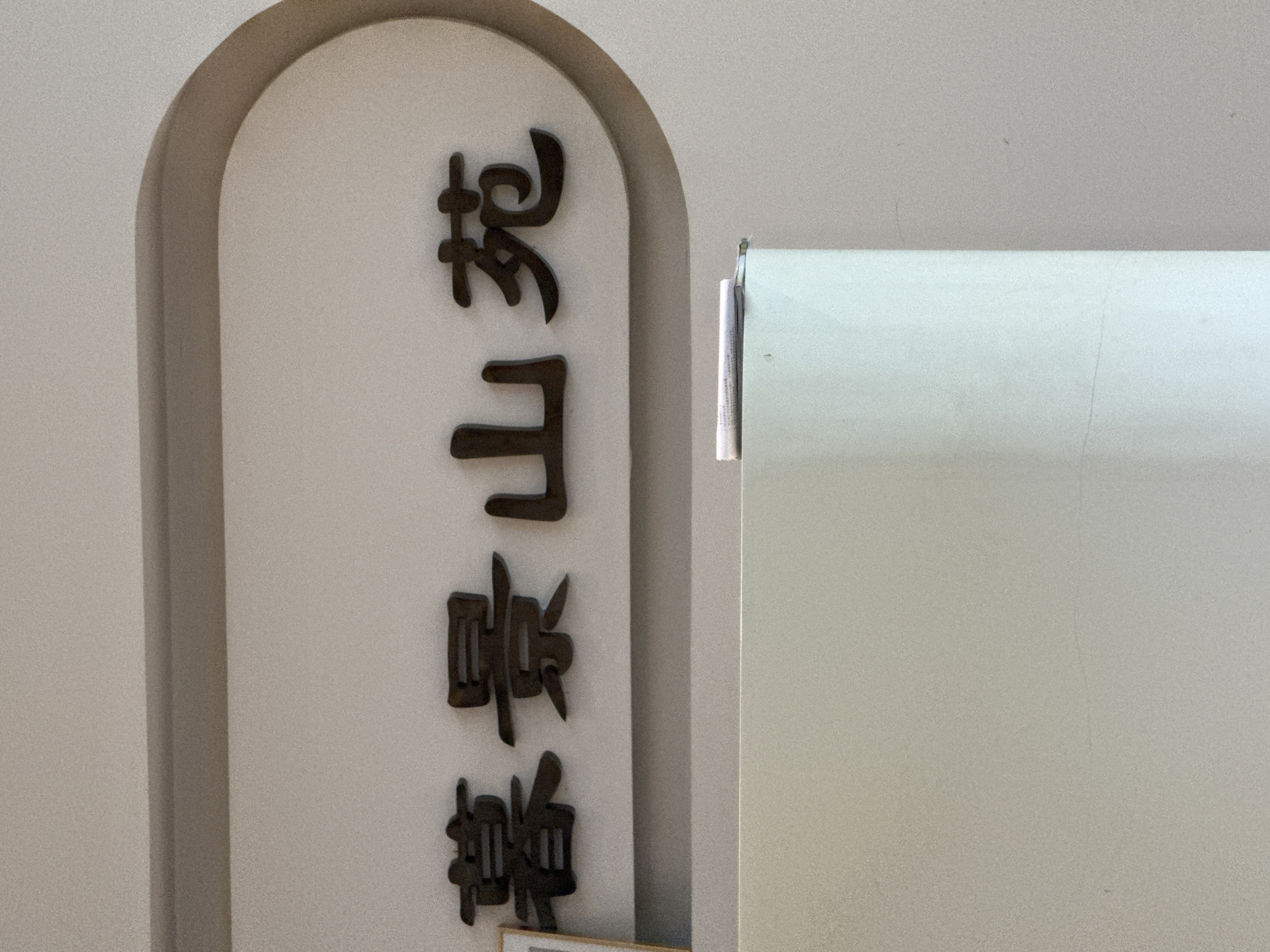 The image shows a vertically oriented sign, likely for a business, displaying Chinese characters in a dark color against a light-colored background. The sign is mounted on a light-colored wall. The characters appear to read, from top to bottom: "岩山薏糖". The sign is partly obscured on the right side by a light-colored panel or door. The location is likely Guilin, China, given the content of the sign.