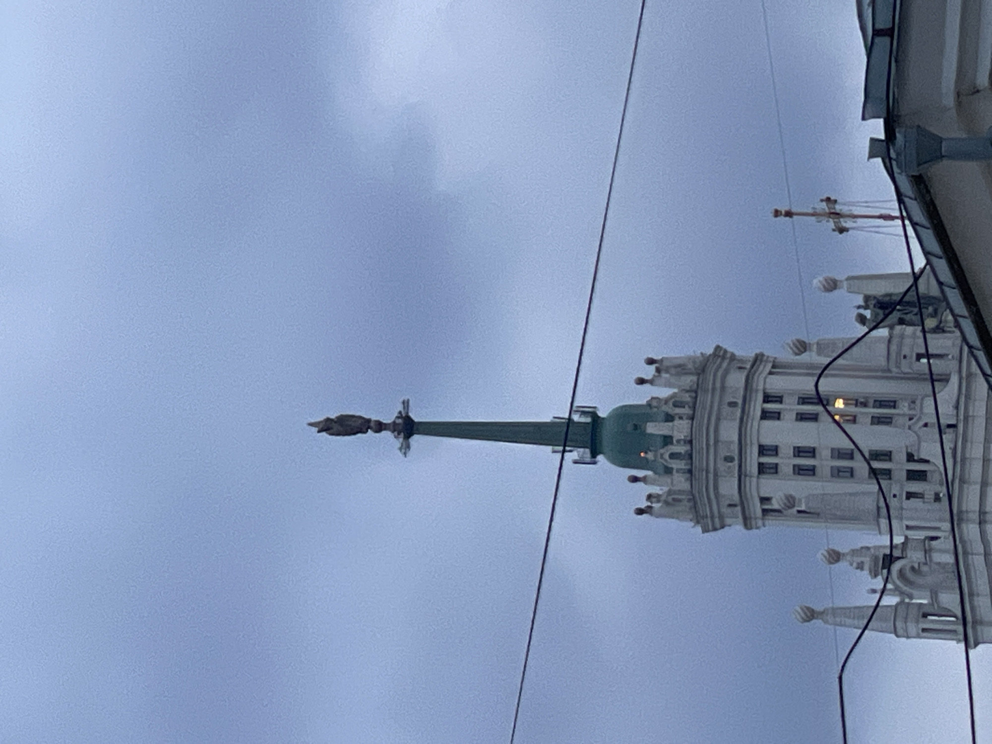 The image shows the Kotelnicheskaya Embankment Building in Moscow, Russia, from a low angle. The sky is overcast. The building's architectural features, including its spire topped with a star, are visible. Overhead electrical wires bisect the view. No people are visible.
