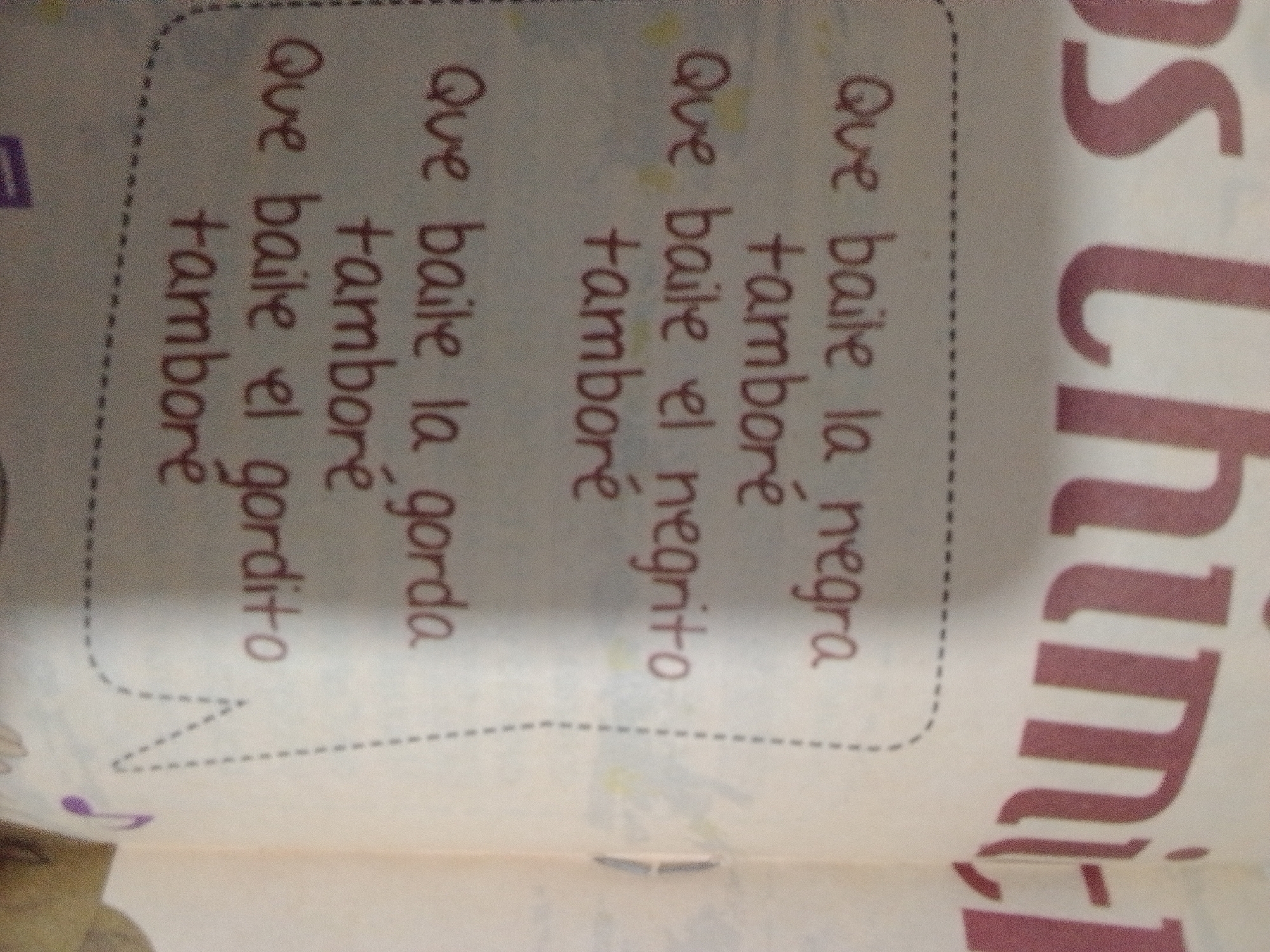 The image displays a piece of paper with text written in Spanish. The text appears to be lyrics or a poem, with repeated phrases like "Que baile la tambore" and "Que baile el gordito." The writing is in a reddish-brown ink and is handwritten. The paper has a dotted line border, suggesting it might be a page from a notebook or a worksheet. There are some faint colored marks or scribbles on the page. The background is a light, textured surface.
Regarding the location of La Tagua, Venezuela, this image does not provide any information or visual cues to suggest it is located there. The image is a close-up of a document and does not depict any outdoor or specific environmental features of a geographical location.