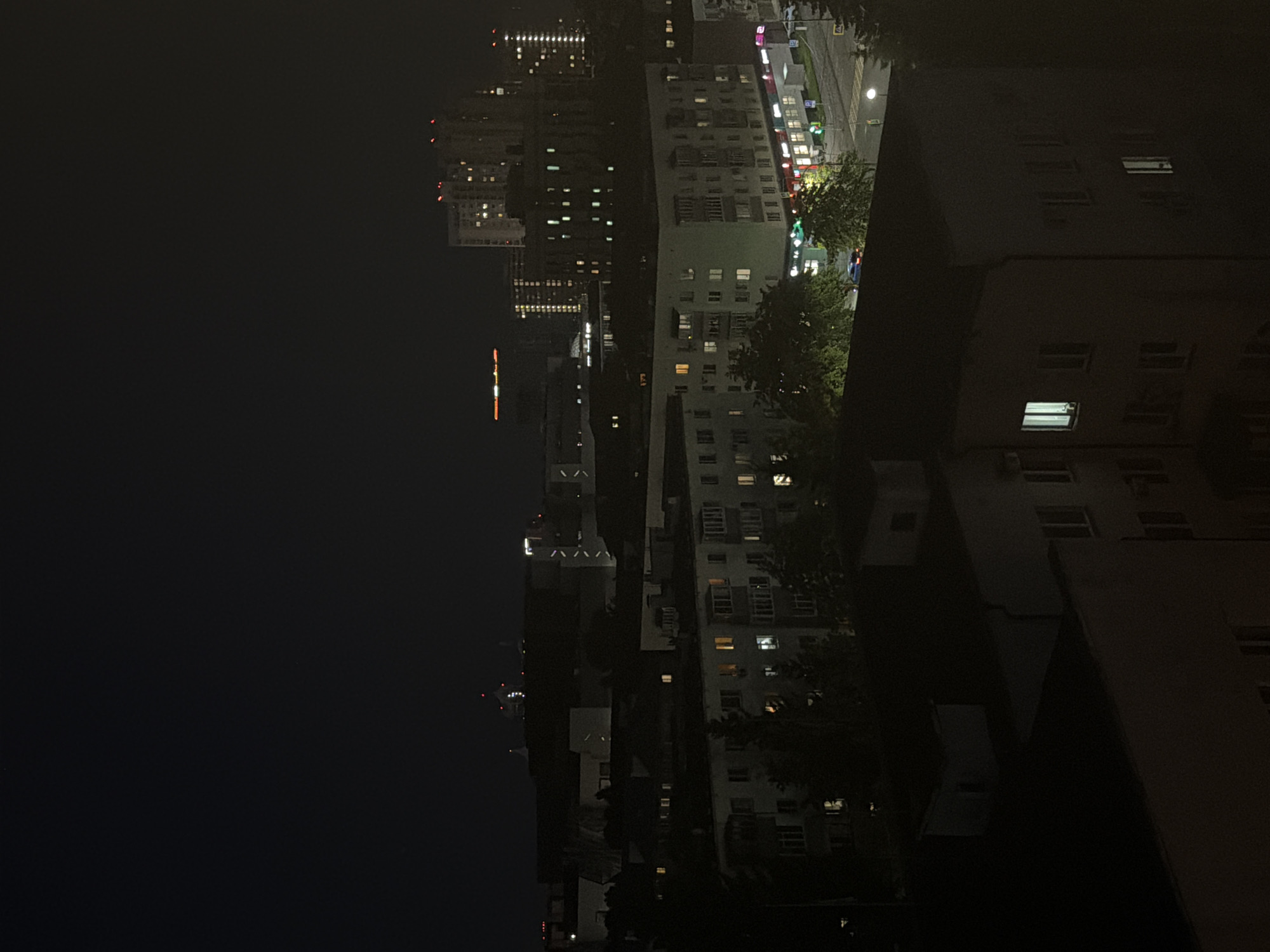This media file shows a nighttime cityscape with tall buildings and a street illuminated by artificial lights. The perspective is from a high vantage point, looking down on the urban environment. The scene is dominated by the dark sky and the glowing windows of residential and commercial buildings. Trees are visible, their silhouettes dark against the illuminated areas. A street with traffic lights and what appears to be a lamppost is also present, suggesting an active urban setting.
The buildings vary in architectural style, with some featuring visible balconies or recessed window frames. The lighting from inside the buildings creates a sense of human presence and activity, even though no people are directly visible. The overall mood is quiet and nocturnal.
The specific location context provided is Kazan, Russia, although no explicit text or universally recognizable landmarks are present in the image to confirm this. The time of day is clearly night, indicated by the darkness of the sky and the artificial lighting. There are no indications of specific weather conditions. The activity taking place is the ordinary functioning of a city at night, with buildings lit and streets potentially in use, though the lack of clear details makes it difficult to ascertain specific events. The image evokes a sense of urban life continuing after dark.