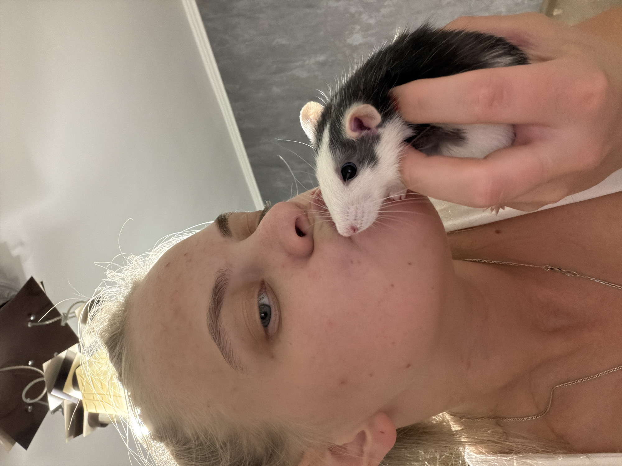 A woman with blonde hair is holding a black and white rat close to her face, appearing to kiss it. The location is Chaikovsky, Russia.