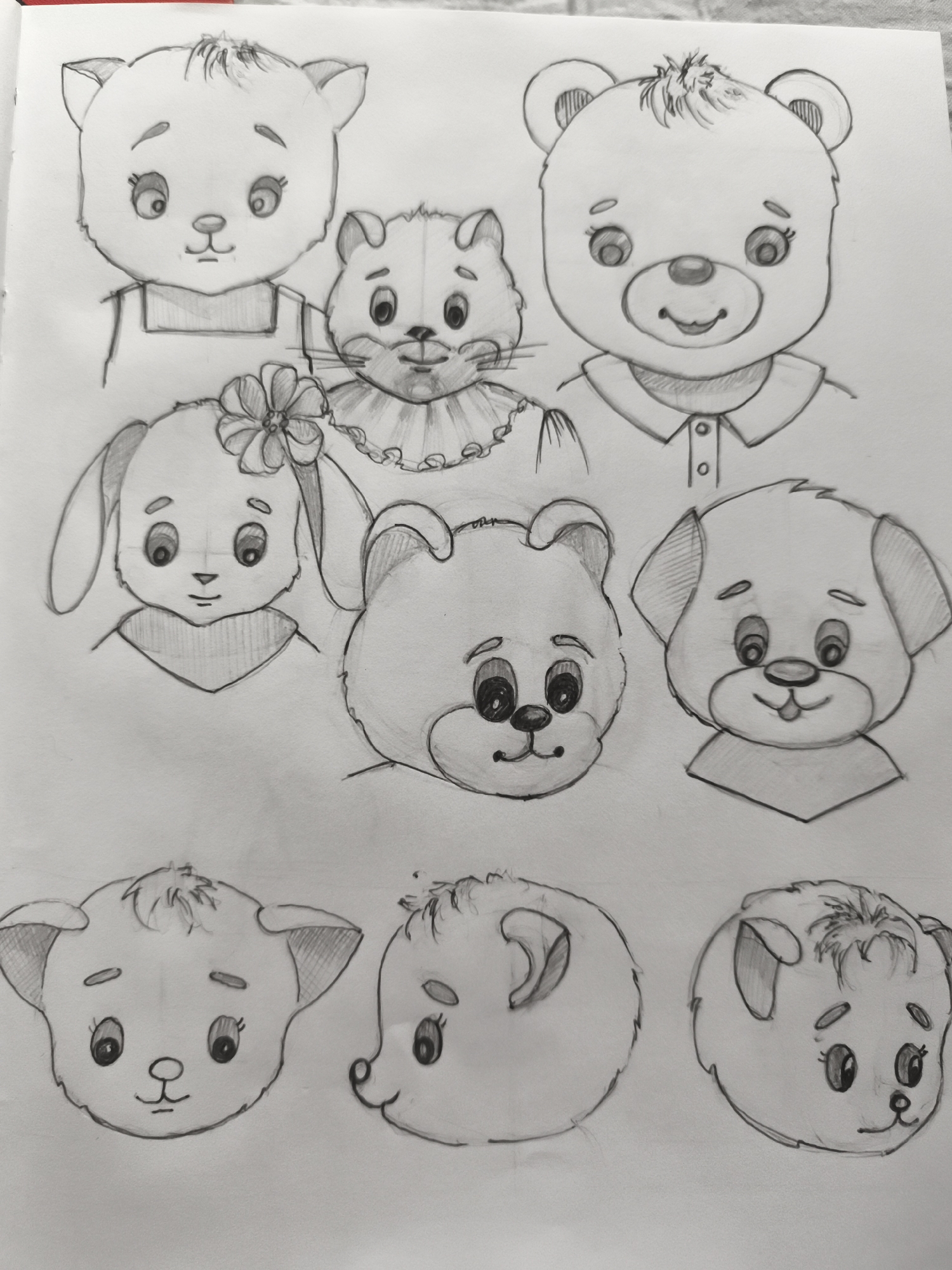 The image is a pencil sketch on white paper, featuring a collection of cartoon-style animal faces. The drawings are arranged in three rows. The top row contains a cat-like face wearing overalls, a smaller cat with a ruffled collar, and a bear face with a buttoned shirt. The middle row shows a rabbit with a flower in its hair, a bear cub face, and a dog face. The bottom row depicts three more animal faces: a cat face, a round-faced animal, and another cat-like face. The sketch is a drawing and does not depict any specific location, including Saint-Denis, France.