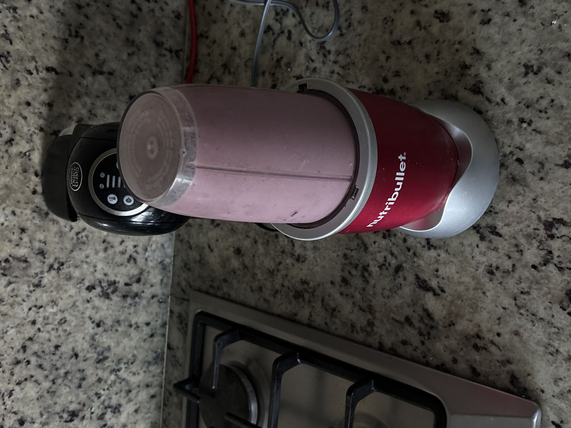 A NutriBullet blender is on a granite countertop in San Bernardino Tlaxcalancingo, Mexico. The blender contains a pink smoothie. A Nespresso coffee machine is partially visible to the left of the blender. A stovetop is in the lower part of the frame.