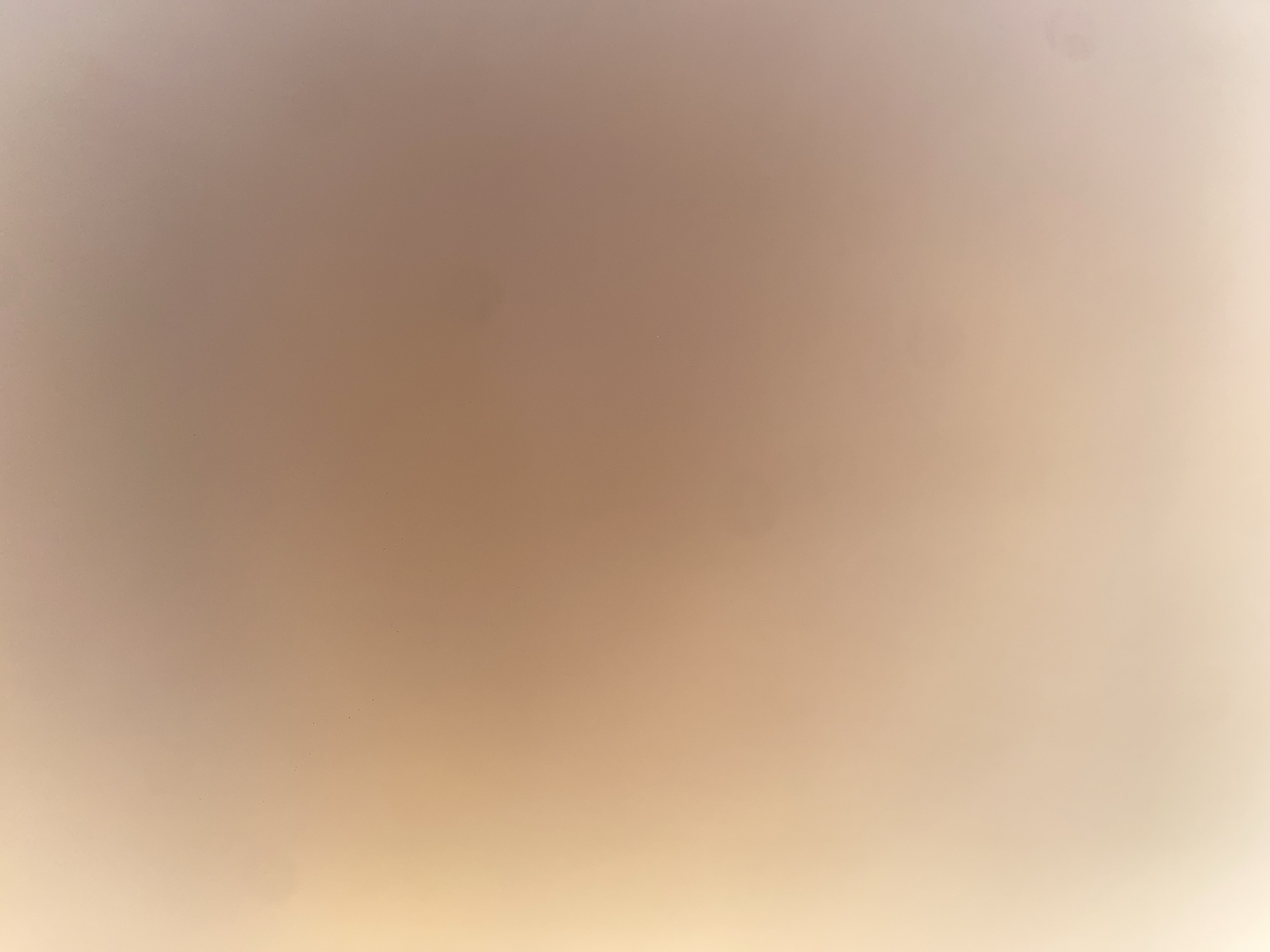 The image is a close-up, slightly out-of-focus shot of a wall. The wall appears to be painted in a gradient of light peach and beige tones, with some subtle darker spots visible, possibly dust or imperfections in the paint. There are no people, objects, or discernible features that would suggest a specific location within the city of Ablanitsa, Bulgaria, or any other identifiable environment. The lighting is soft and diffused, creating a smooth, almost abstract appearance.
