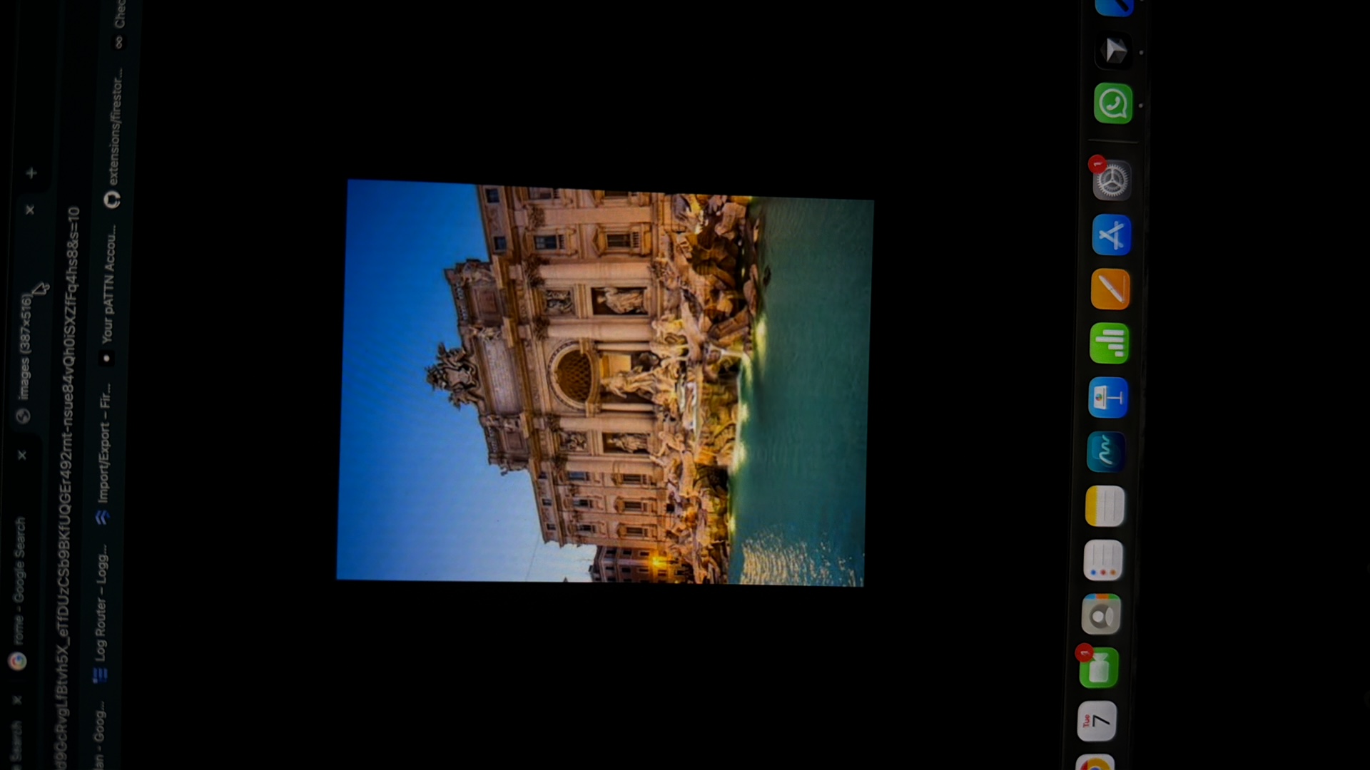 The image displays a screenshot of a web browser with a photograph of the Trevi Fountain in Rome, Italy, as the main subject. The browser tabs show searches related to "rome - Google Search" and "images (387x516)". Below the tabs, a URL is partially visible, and other browser tabs show links to "Log Router," "Import/Export," and "Your pATTN Accou...". The bottom of the screen shows a dock with various application icons, including a calendar, mail, and a phone symbol with a notification. The photograph itself is a well-lit, angled shot of the Trevi Fountain at dusk or night, showcasing the intricate sculptures and the illuminated water. The city of Kafr Yasif, Israel, is not depicted or mentioned in this image.