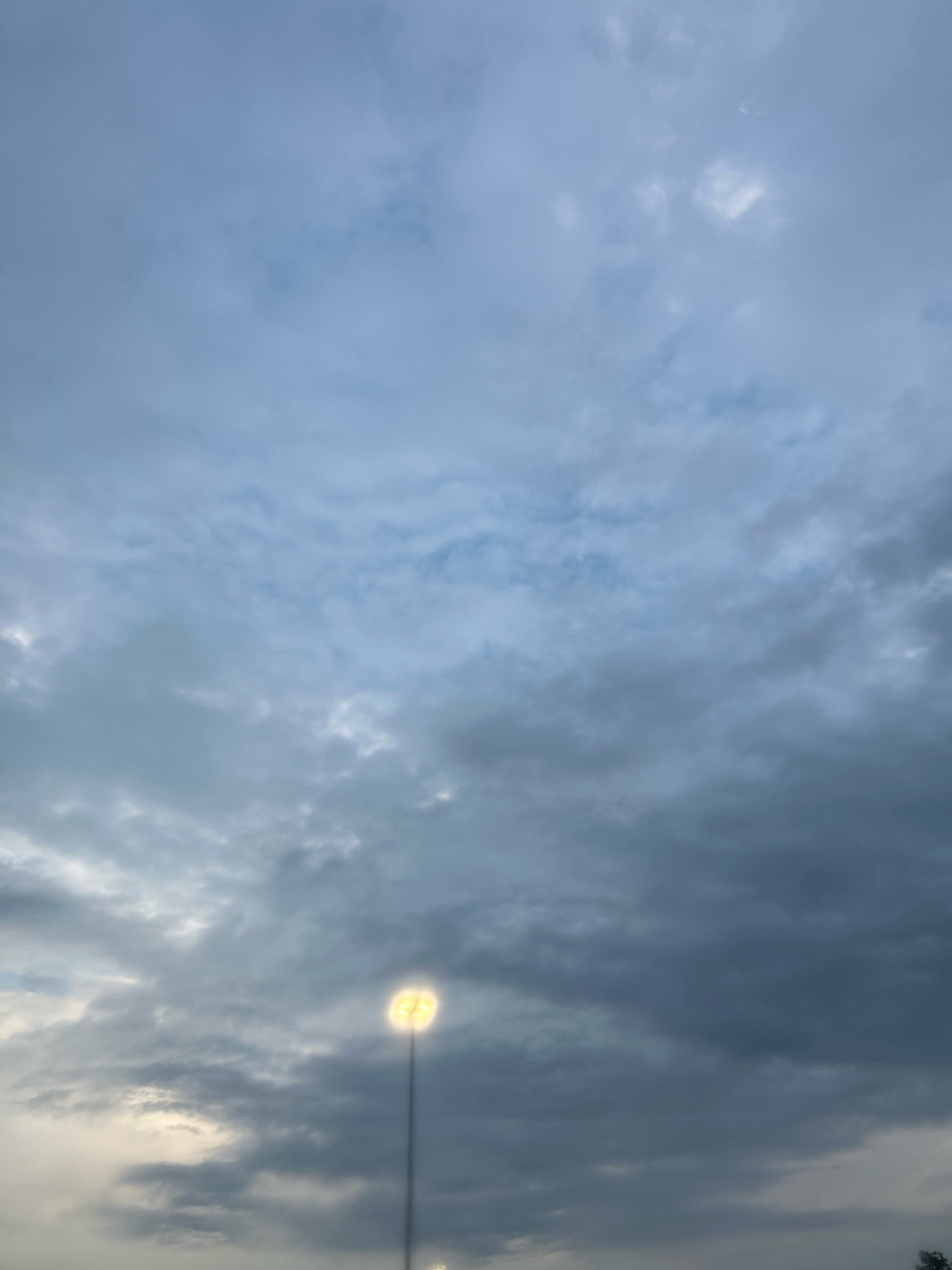 The image shows a dusky sky with heavy clouds, the light from a streetlamp shining brightly on the right side. The streetlamp is tall and thin, with a round, glowing light at the top. The sky is a mix of dark gray and lighter blue, with some patches of white clouds. The overall impression is one of a moody, atmospheric evening. The image appears to have been taken in Robinson Township, United States of America.