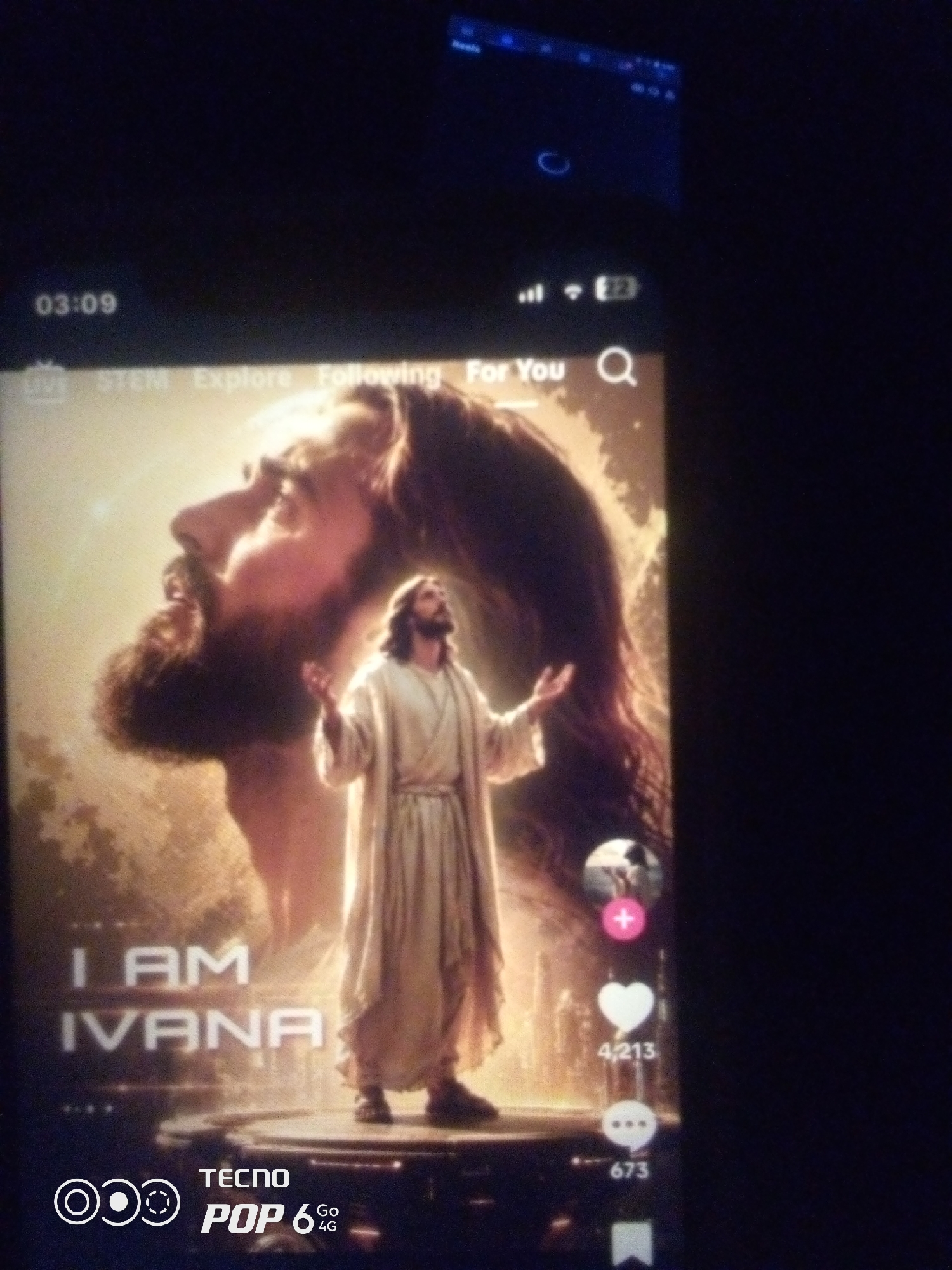 The image shows a screenshot of a TikTok video. The video features a depiction of Jesus Christ, with a large, stylized image of his face in the background and a smaller figure of him in the foreground, arms outstretched. Text overlays on the video read "I AM IVANA". On the right side of the screen, there are icons for liking, commenting, and sharing, with numbers indicating likes and comments. In the bottom left corner, there is a Tecno Pop 6 4G logo. The image is of low quality with significant digital noise, and it is difficult to ascertain the precise location within Howayi, Nigeria, as the image appears to be a screenshot of a mobile device displaying content rather than a photograph taken in a specific outdoor or indoor environment in the city. The time stamp on the top left corner shows "03:09".