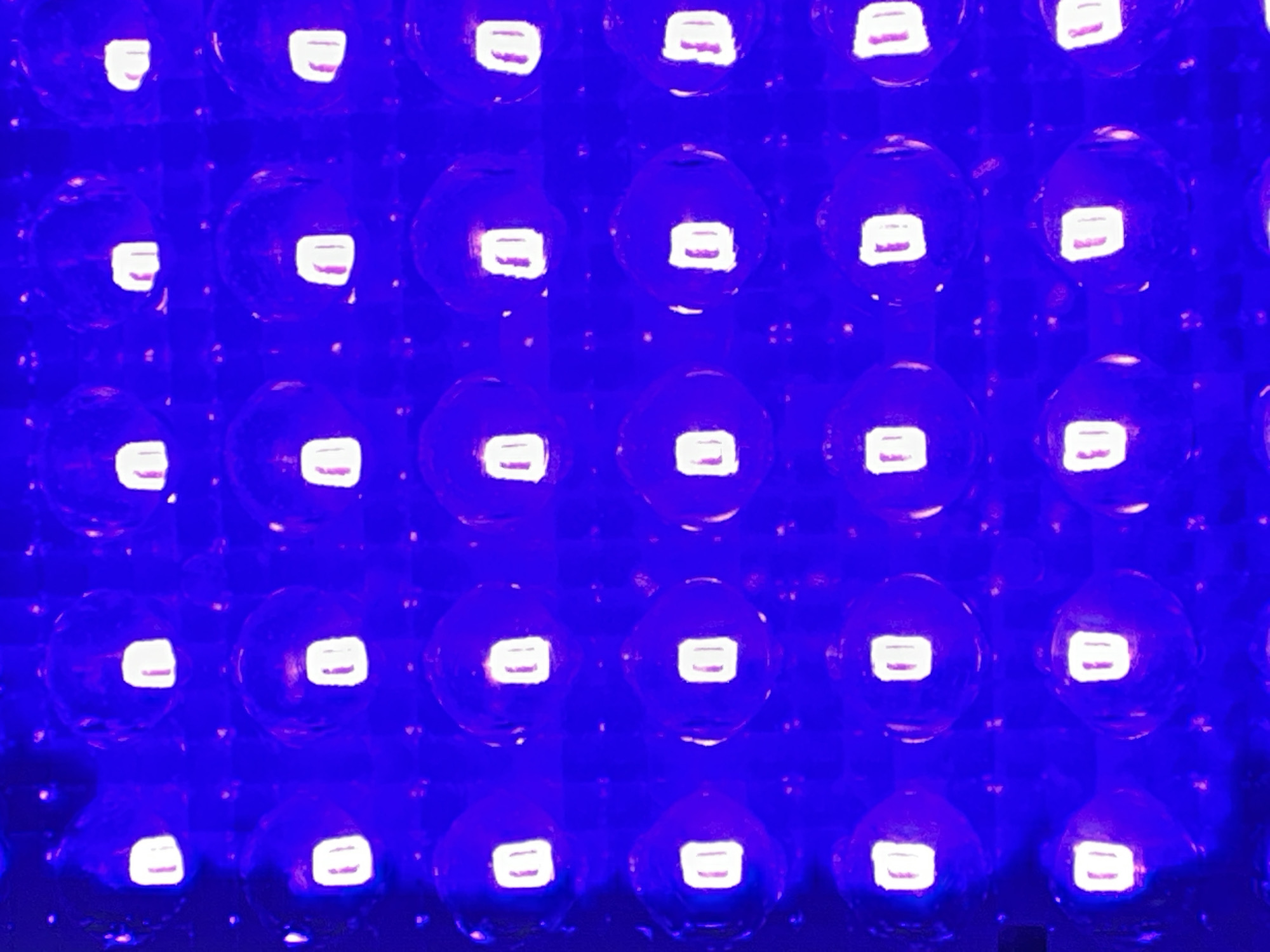The image shows an array of circular blue lights, possibly LEDs, arranged in a grid pattern. Each light appears to have a brighter, rectangular center. The background appears dark. There is no location, city, or other contextual information present in the image.