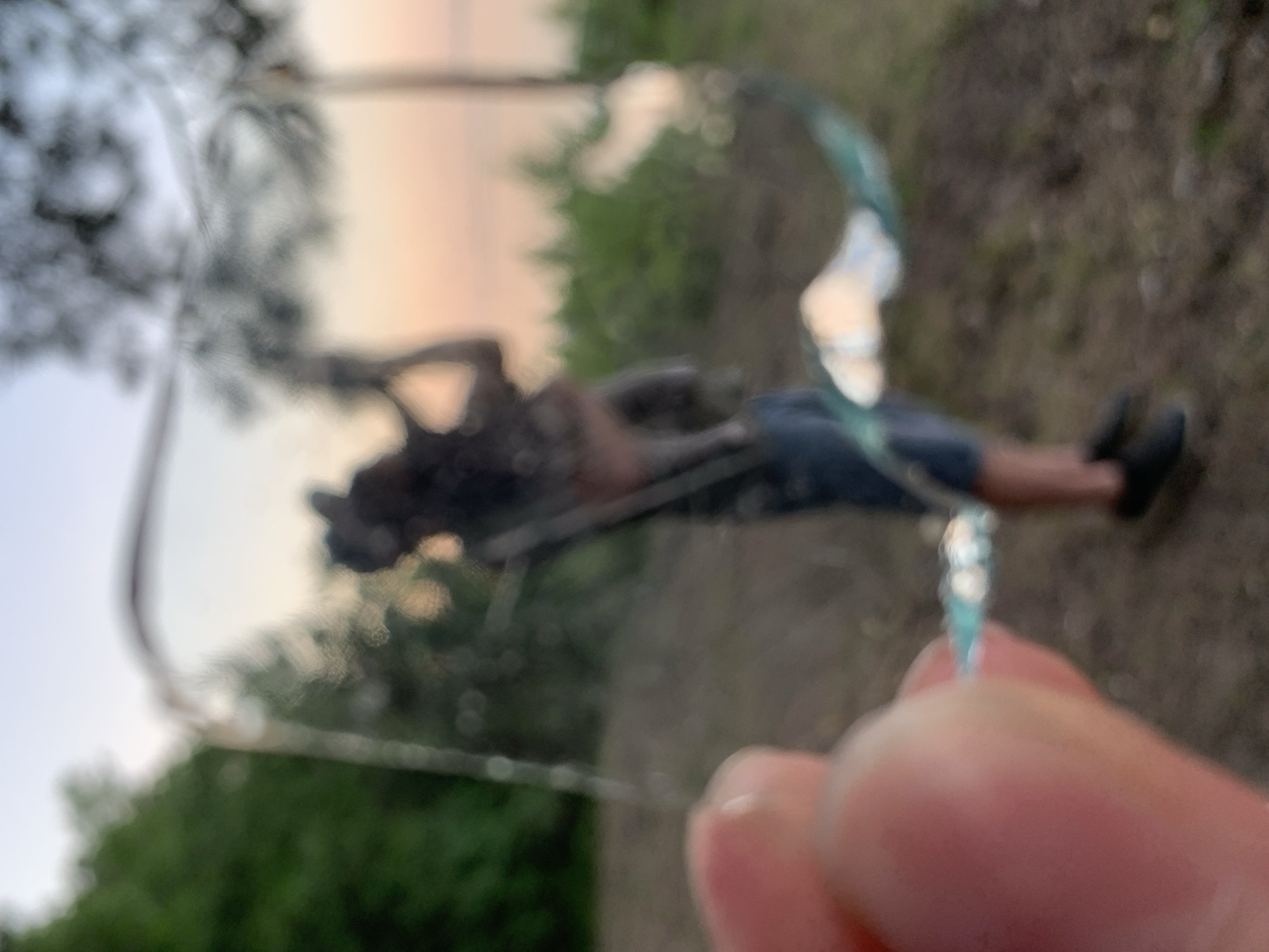 A person is lying down on the ground, seemingly reflected through a broken pane of glass held up in the foreground. The background suggests an outdoor environment with greenery and a light sky. The photograph is taken in a blurry, amateur style, and the location is possibly Chaikovsky, Russia.