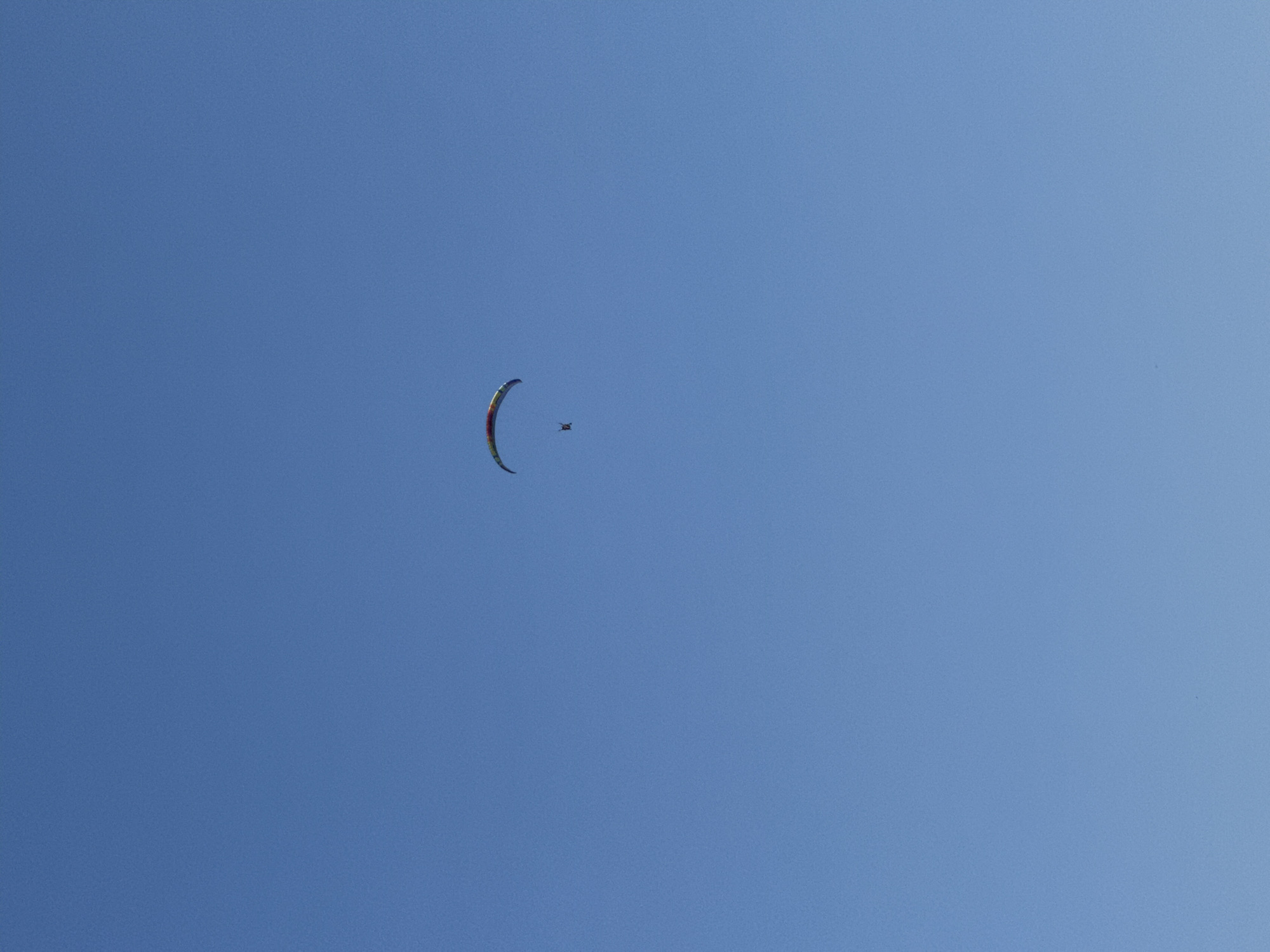 In the clear blue sky above Boreti, Montenegro, a paraglider is captured mid-flight. The paraglider, with a colorful wing, appears as a small object against the vast expanse of the sky, with a person visible beneath the wing.