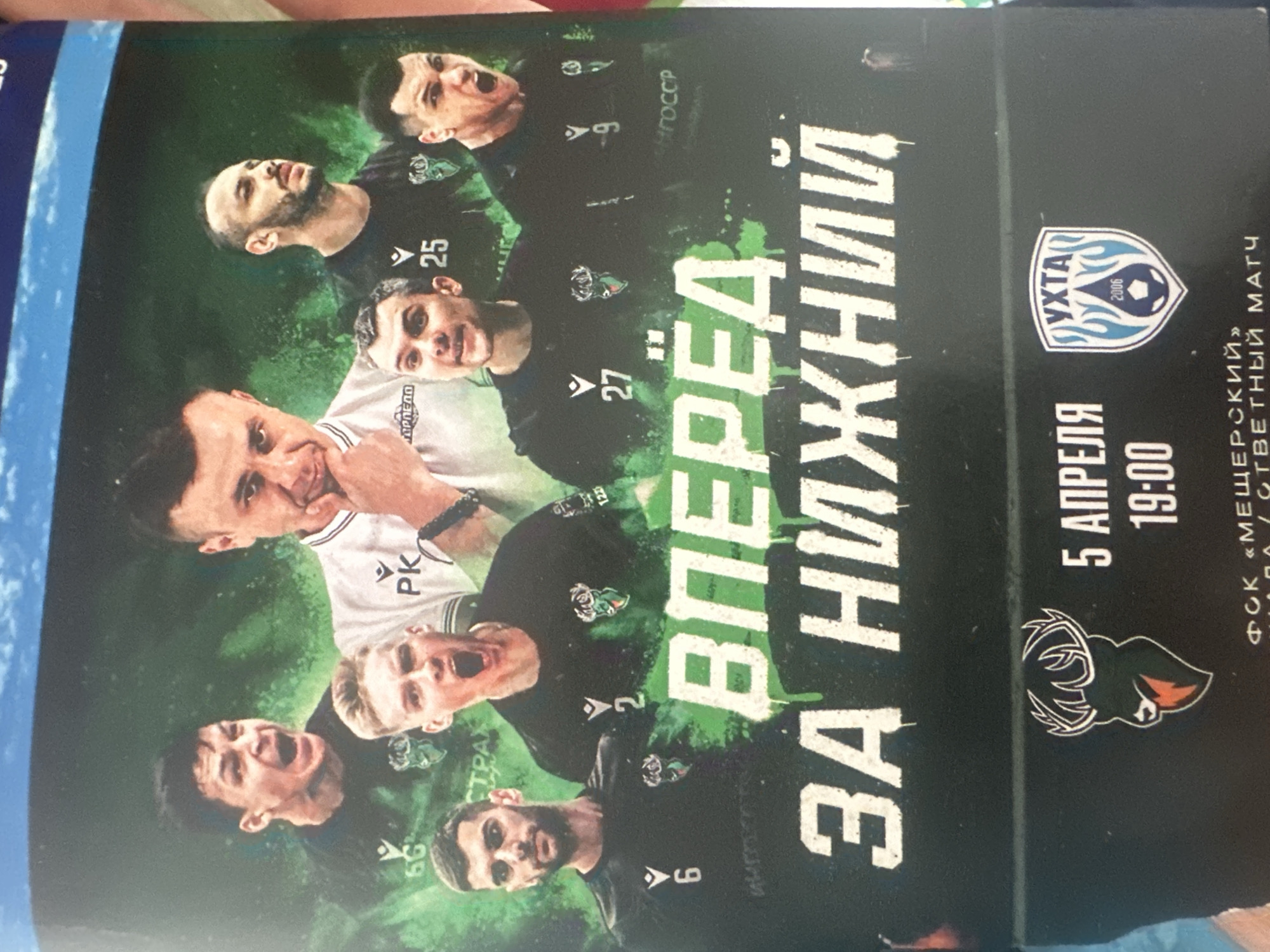This image is an advertisement for a sports event, featuring a montage of seven male figures, presumably a sports team and their coach, against a dark green and blue background.
The upper portion of the background displays a light blue sky with faint white cloud formations, transitioning into a vibrant, mottled dark green and black abstract pattern that covers the central area where the figures are positioned.
In the foreground, seven men are arranged in a dynamic composition. At the top center, a man with short dark hair, wearing a white polo shirt with "PK" and a logo on the left chest, looks thoughtfully towards the viewer, with his right hand touching his chin. Surrounding him are six other men, wearing dark green or black long-sleeved jerseys with a white 'V'-shaped logo (Macron) and a deer-head emblem on the left chest. Several players have their mouths open in expressions of shouting or roaring, indicating intensity. From left to right: a player with dark hair on the upper left, jersey showing "6G"; a player with a beard on the mid-left, jersey number "6"; a player with light hair in the center, jersey number "2"; a player with a beard on the mid-right, jersey number "25"; a player with graying hair on the bottom-center, jersey number "27"; and a player with dark hair on the bottom-right, jersey number "9". Sponsors or other text are partially visible on jerseys, including "СТРАХ" and "ГОСС", and "ТОРПЕДО" on the coach's shirt.
Large, dripping white letters across the bottom half of the image spell "ВПЕРЕД ЗА НИЖНИЙ" (FORWARD FOR NIZHNY).
Below this text, on a solid black bar, the deer-head logo is prominently displayed on the left. To its right, the date "5 АПРЕЛЯ" (5 APRIL) and time "19:00" are shown in white text. Further to the right, a blue and white shield logo for the opposing team, "УХТА" (UKHTA) with "2006" and a soccer ball icon, is present. The very bottom of the image, partially obscured, indicates the location as "ФСК «МЕЩЕРСКИЙ»" (FSK "MESHCHERSKIY") and mentions "/ ОТВЕТНЫЙ МАТЧ" (RETURN MATCH).
The event is scheduled for April 5th at 19:00 at the Meshchersky Sports Complex in Nizhny Novgorod, Russia.
