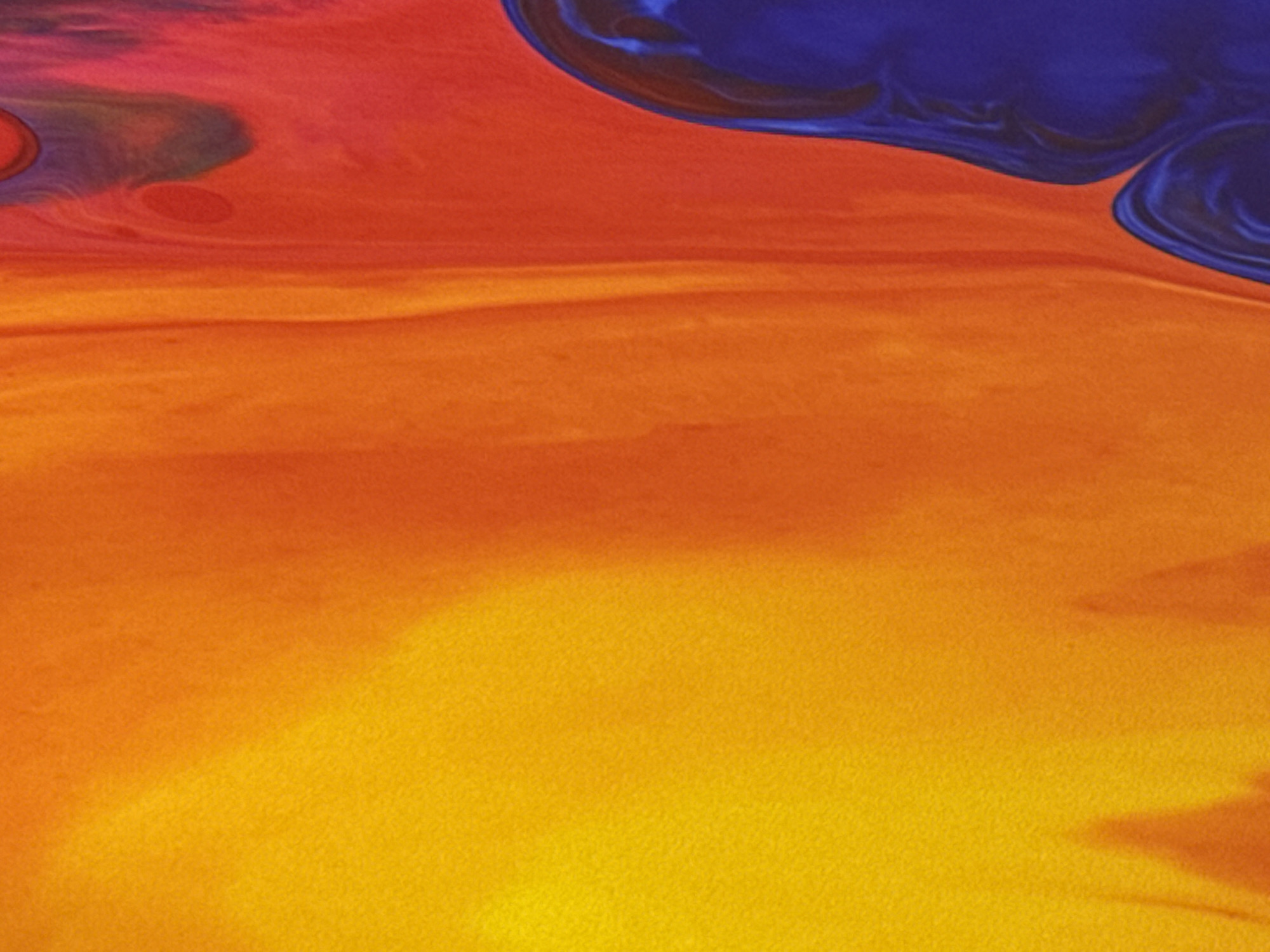 This is an abstract image of liquid paint marbling in vibrant colors, primarily orange, yellow, red, and blue. The texture appears to be granular, resembling canvas or textured paper. There are no discernible figures, objects, or environmental elements that can be located in any specific city, including Tallinn, Estonia. The image is purely an abstract composition of color and texture.