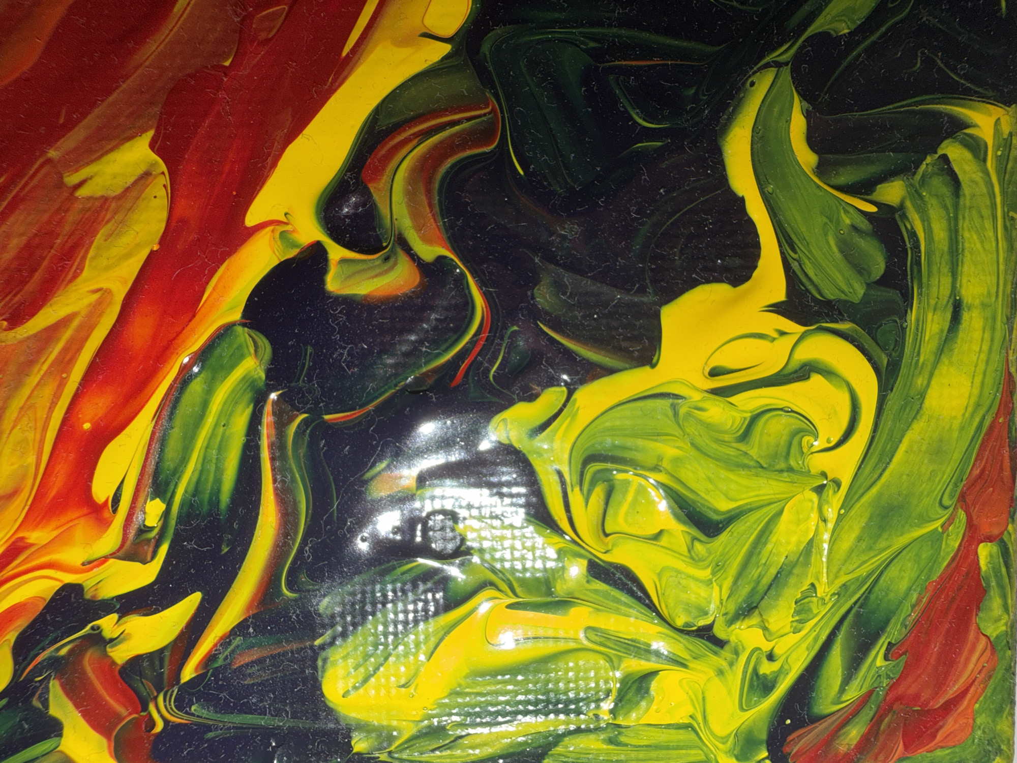 This is an abstract, close-up photograph of acrylic paint being swirled and blended on a surface. The colors are predominantly red, yellow, and various shades of green, with areas of dark, deep black. The paint is thick and appears to have been applied with a palette knife or similar tool, creating visible texture and ridges. There are streaks and swirls of color, with some areas showing a glossy, wet appearance and others appearing more matte and slightly cracked. The overall impression is dynamic and organic, with no discernible objects or figures. The image does not depict any location in Nha Trang Ward, Vietnam, or any specific scene.