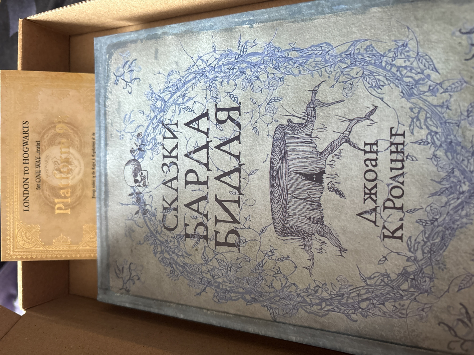 The image shows two books in a cardboard box. The book on the left has the text "LONDON TO HOGWARTS" and "Platform" on its cover. The book on the right has text in Russian and the name "Джоан К. Ролинг", which is "Joanne K. Rowling" in Russian. Both books are presumably inside a cardboard box. The image does not contain information about the city of Lukintsy, Russia, or any people, subjects, actions, or interactions beyond what is depicted on the book covers and their placement in the box.
