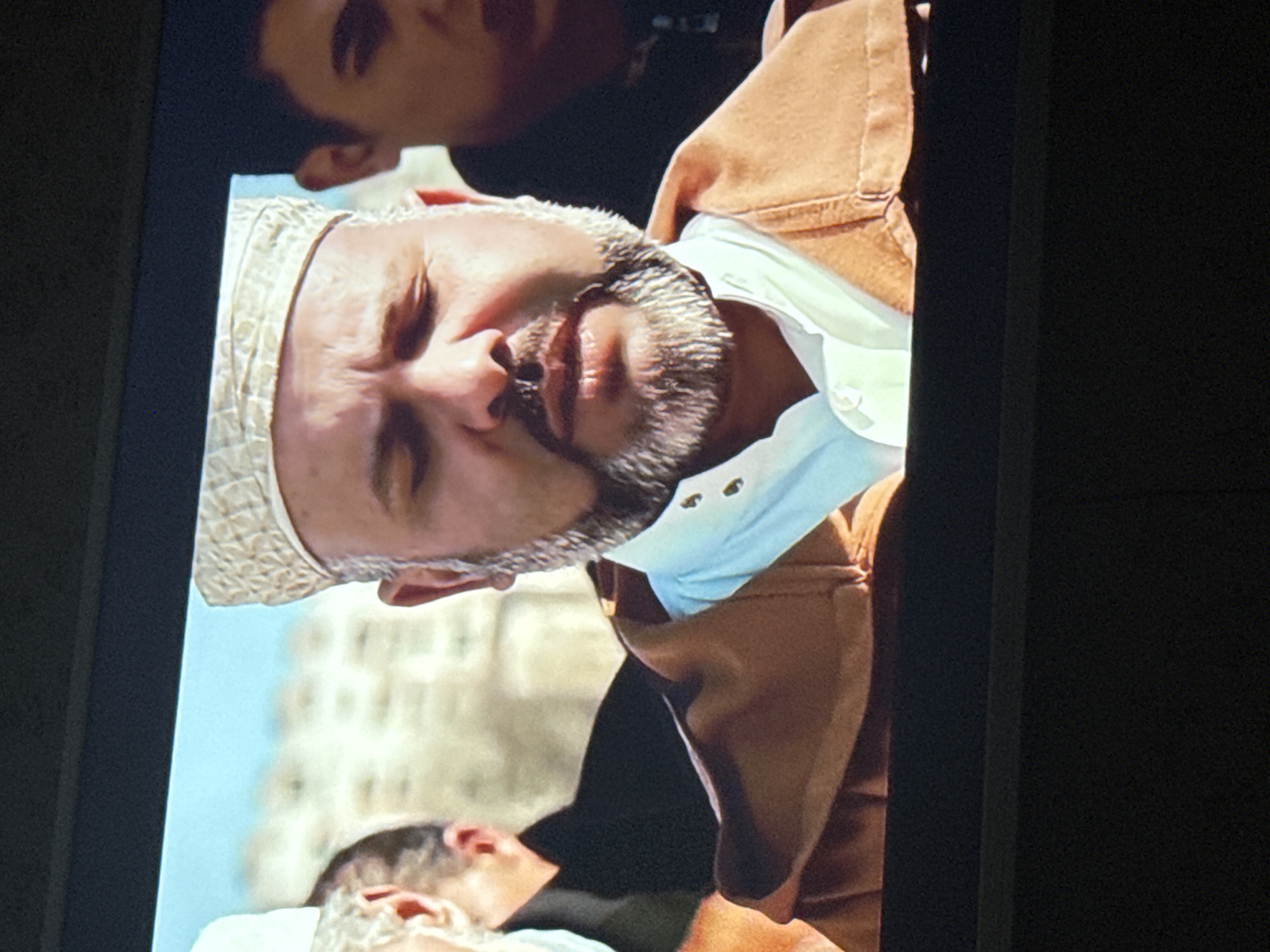 A headshot of King Mohammed VI of Morocco wearing a white kufi is visible. He is wearing a white shirt and a tan jacket. Another person is visible above him and a third person is below him. They are outside with a building in the background. There is no indication the location is Mytishchi, Russia.