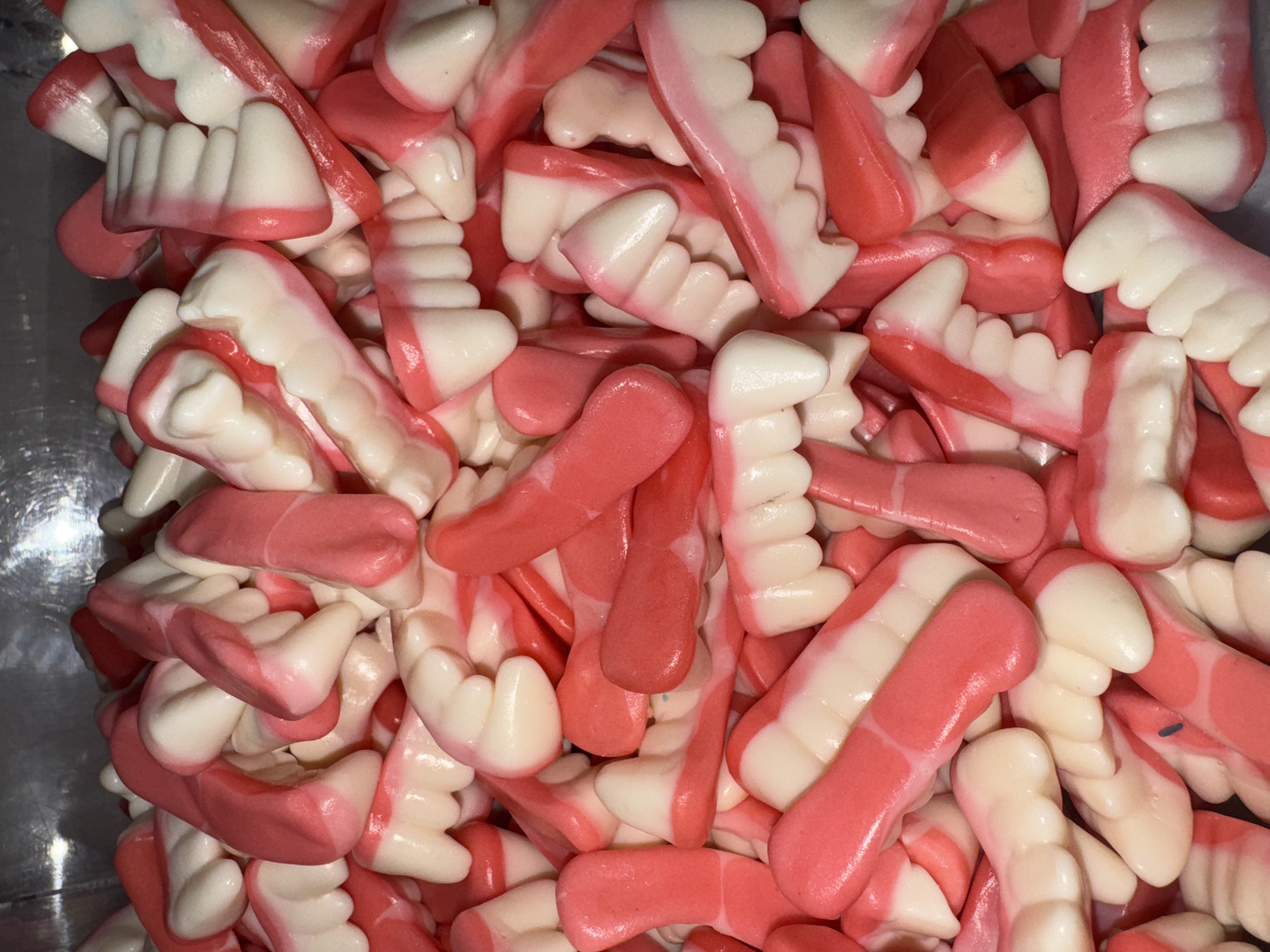 The image shows a dense pile of gummy candies shaped like sets of teeth and gums. The "teeth" are white, and the "gums" are pink. The candies fill the entire frame, creating a textured and colorful composition. There is no indication of Saint Petersburg, Russia in the image.