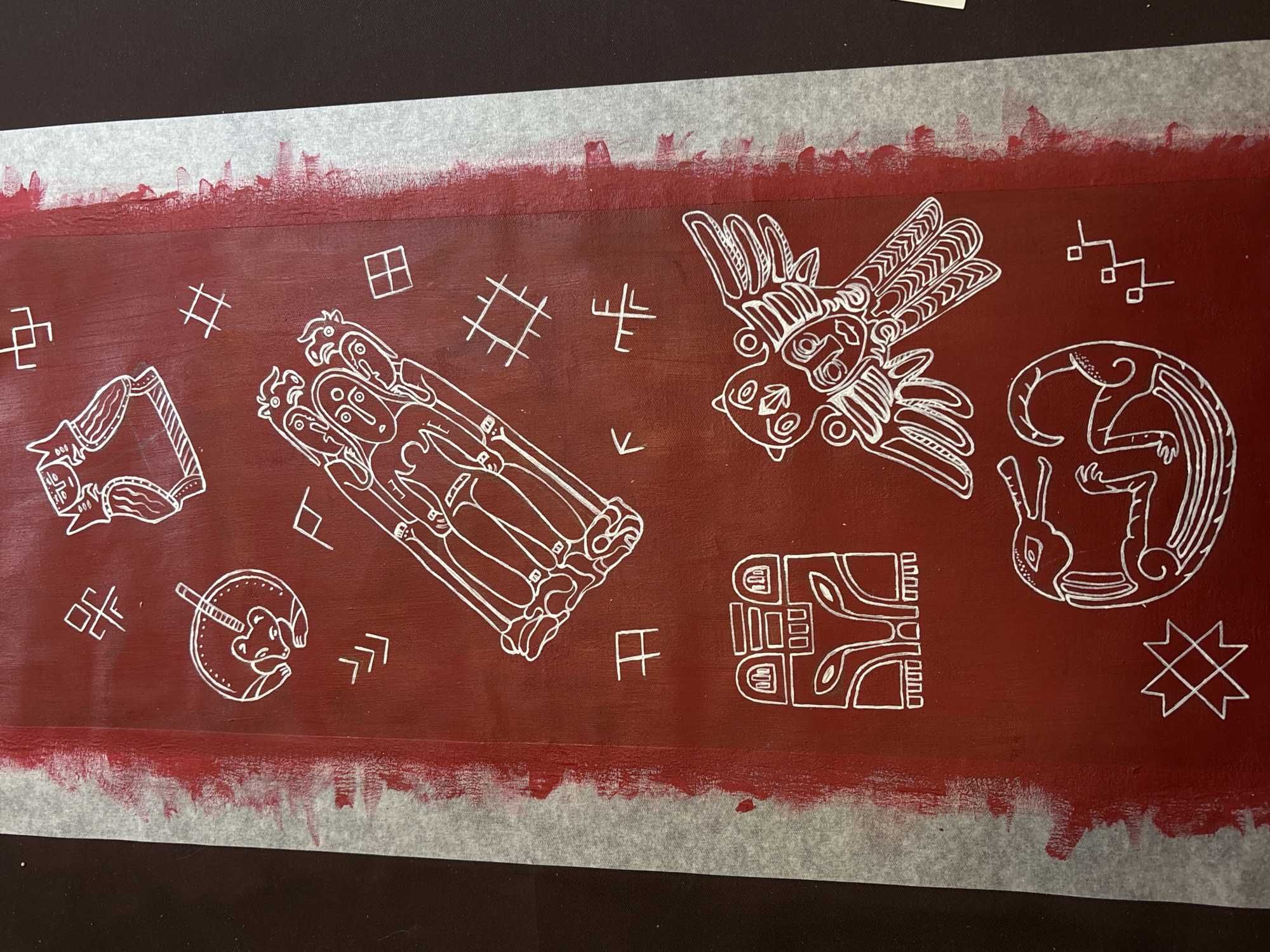 The image shows a reddish-brown canvas with white drawings inspired by Permian animal style art, a distinctive artistic style from the region of Perm, Russia. The drawings include stylized animal figures such as a bird, a human-animal composite, and other geometric and symbolic shapes characteristic of the Permian cultural tradition. The canvas is bordered with a strip of white painter's tape. It sits against a black surface.