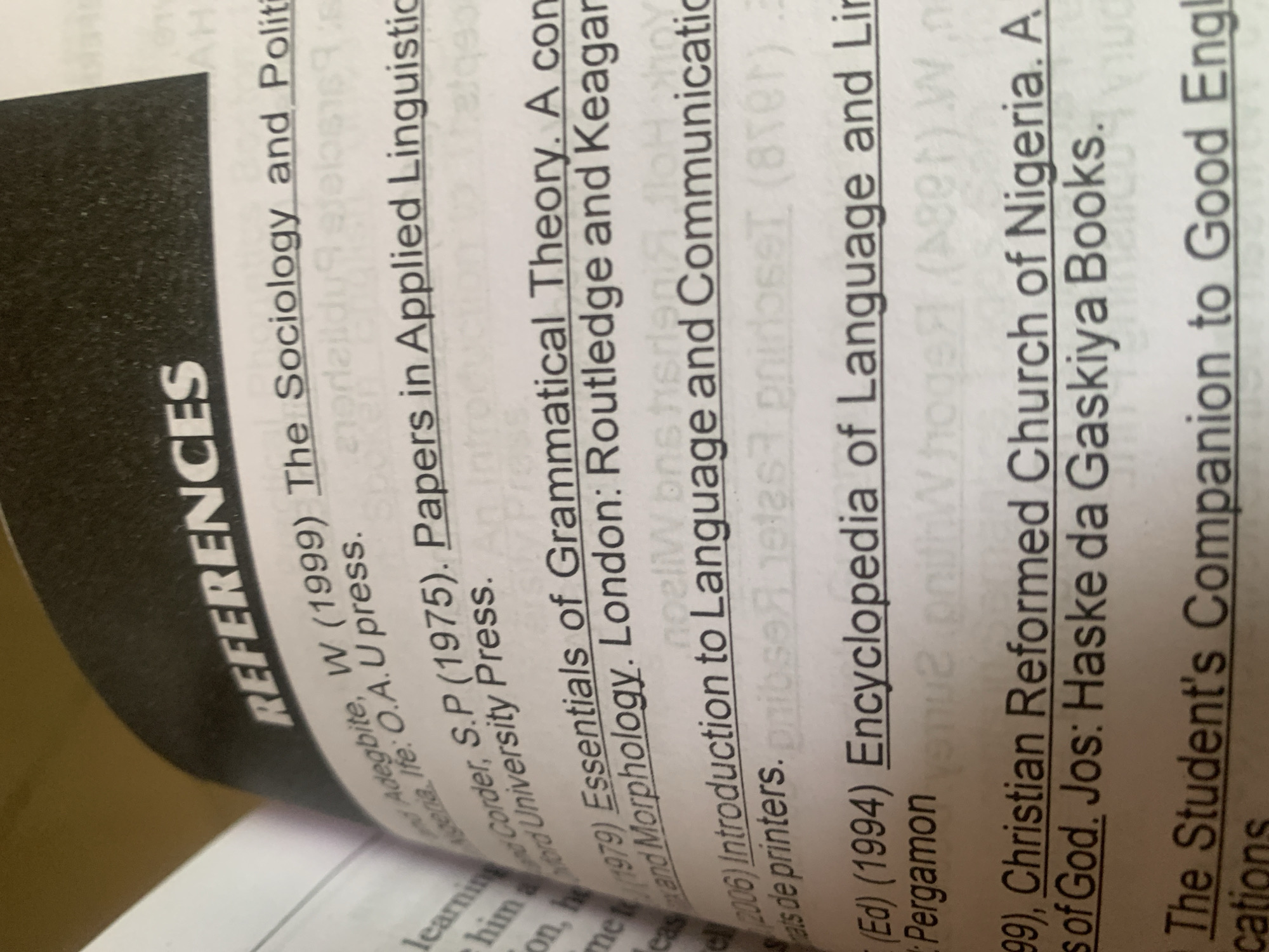 The image shows a page from a book, with the heading "REFERENCES" in large, bold, white font against a black background. Below the heading are several bibliographic entries, suggesting the book is an academic text. The entries are formatted in a standard citation style, including author names, publication years, titles, and publishers. Some of the entries mention locations such as London and Nigeria. The text is clear and readable, indicating a well-printed book. There are no people or specific actions depicted in the image; it is a still life of a book page. The environment is implied to be an indoor setting, consistent with a library or study. The content of the references relates to linguistics and sociology. There is no information in the image that places it in the city of Jauro Yinu, Nigeria, or any other specific city.