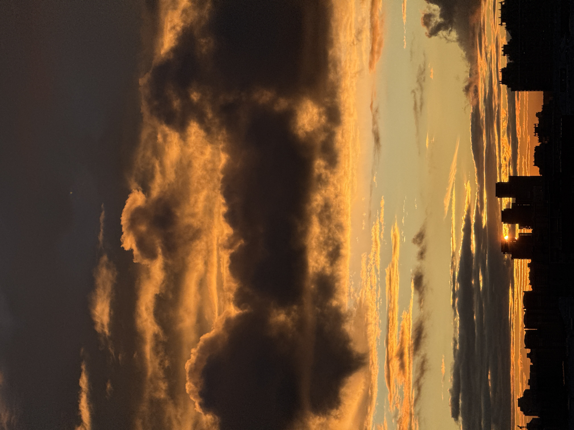 The image depicts a sunset over Moscow, Russia. The sky is filled with golden and dark clouds. In the foreground, the silhouette of buildings is visible. The sun is setting behind the buildings.