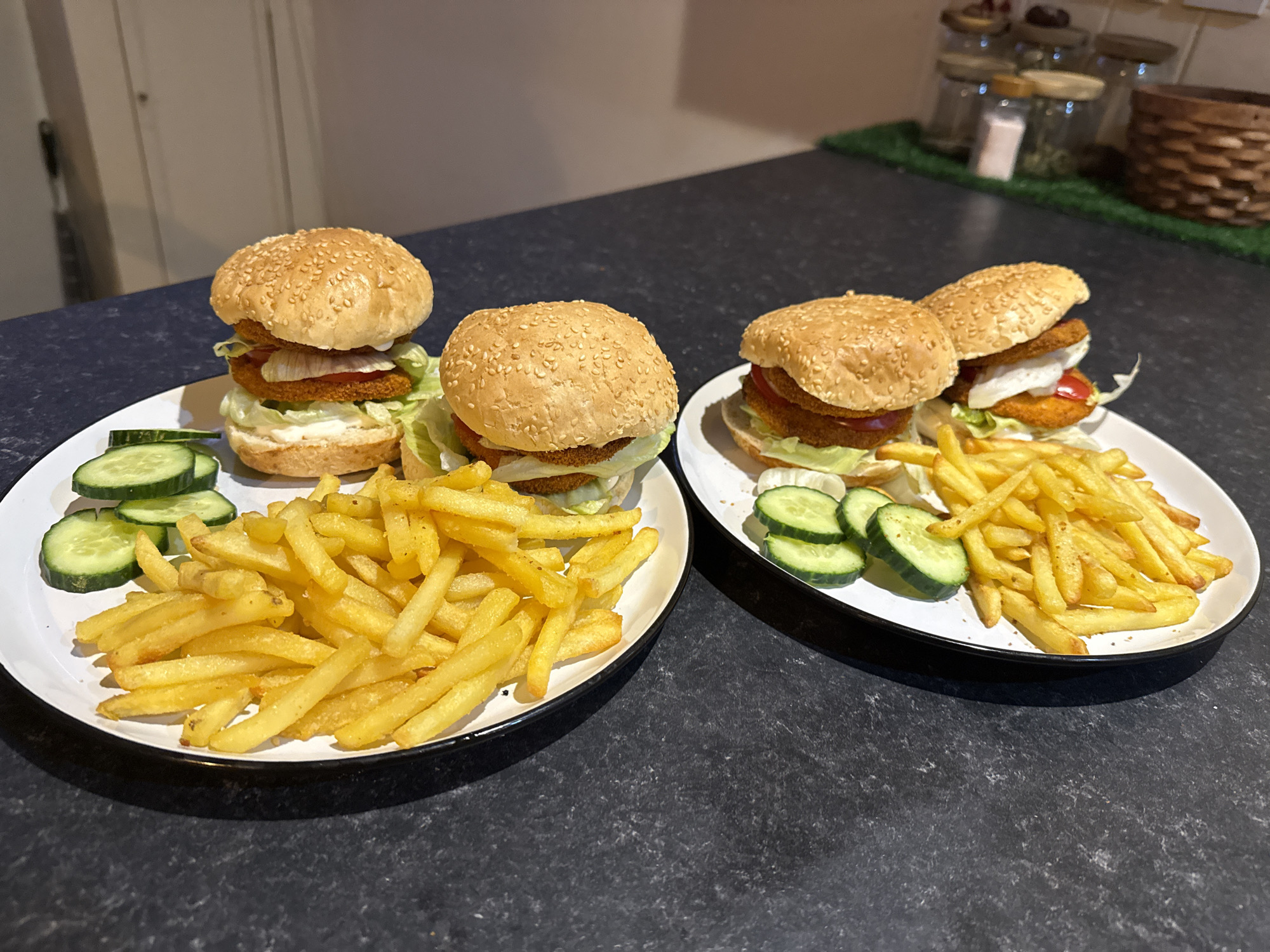 The image shows two plates of food. Each plate contains one and a half burgers, french fries, and sliced cucumbers. The burgers are on sesame seed buns and appear to contain lettuce, tomato, and a fried patty. The location is unknown, and no information about the city of Great Yarmouth, United Kingdom, is discernible.