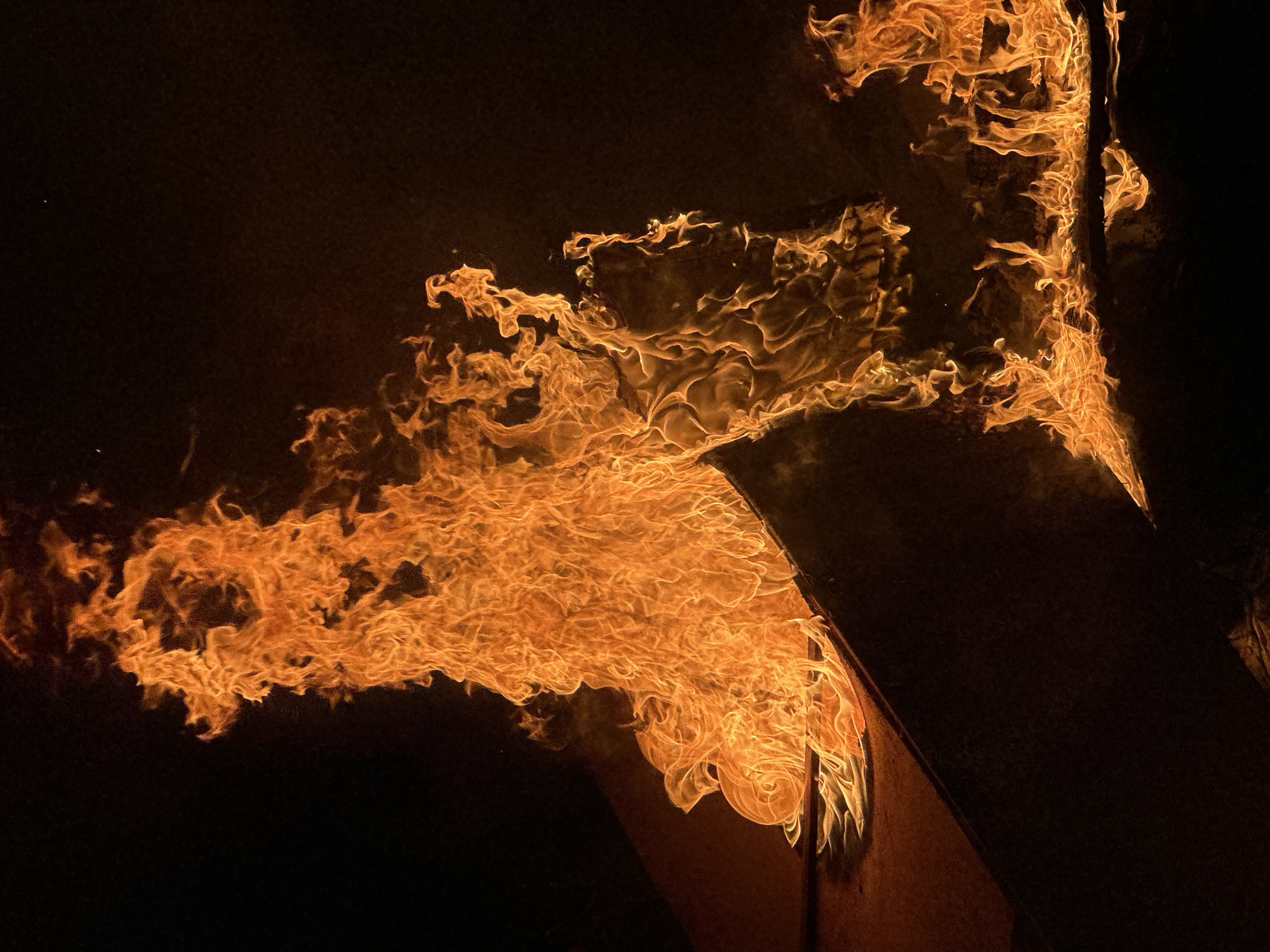The image depicts flames engulfing an object in a dark environment. The fire is predominantly orange and yellow, with tendrils reaching upwards and outwards. The object appears to be metallic and angular, possibly part of a structure. The location is Bac Nha Trang Ward, Vietnam.