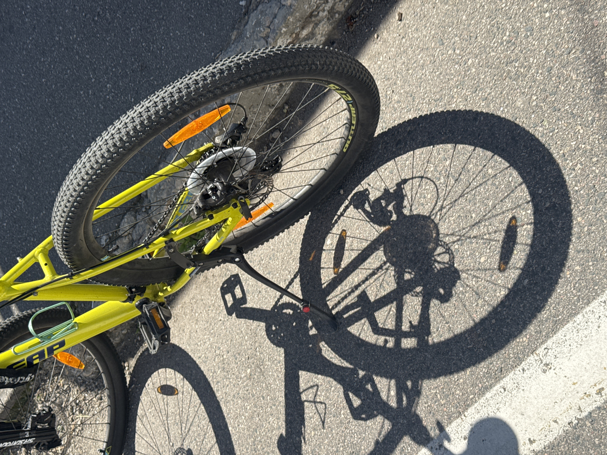 A yellow bicycle lies on its side on asphalt, casting a detailed shadow of its wheels, frame, and pedals. The setting appears to be outdoors on a sunny day. The exact location of Saratov, Russia is not determinable from this image.