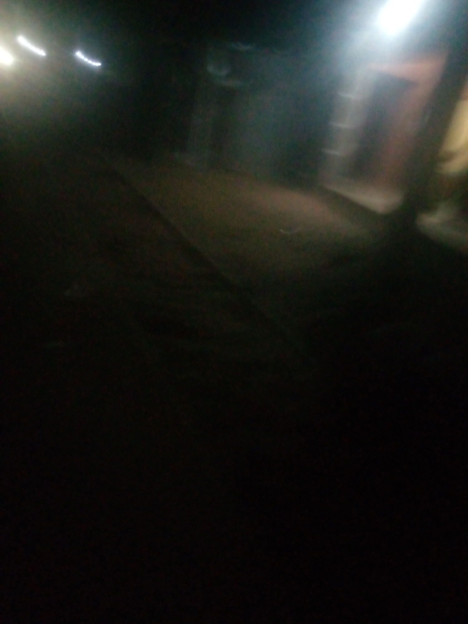 The image captures a dark, blurry scene that appears to be a street at night, possibly in Jalingo, Nigeria. Streaks of light suggest movement, possibly from vehicles or a handheld camera. In the background, a dimly lit building with horizontal elements, possibly stairs or windows, is visible. The overall impression is of a low-light, possibly unstable recording, making specific identification of people or objects difficult.