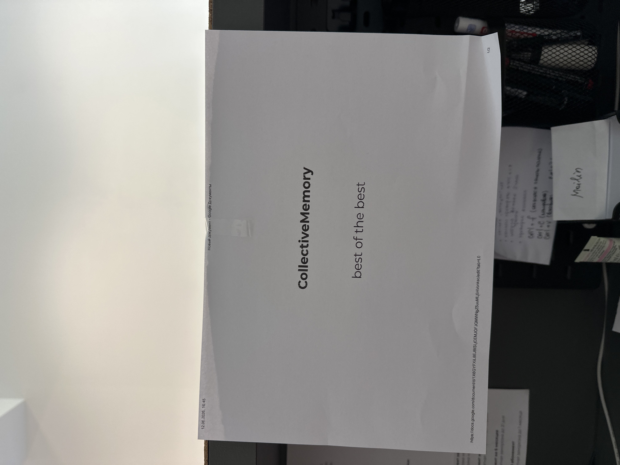 The image displays a sheet of paper with text printed on it, which is taped to a surface. The paper shows "CollectiveMemory" in large font, and "best of the best" in smaller font below it. In the top left corner of the paper, the date "12.06.2026, 16:45" is visible. In the top right corner, the text "Новый документ - Google Документы" is present. A URL, "https://docs.google.com/document/d/1X6GYFXIL8EJ8ISLJCCMJOFJQMWNgZ5uuMLJ9AVonKsc/edit?tab=1.0", is printed near the bottom of the sheet. The paper is positioned on a dark surface, which appears to be a desk or table. To the right of the paper, a black mesh container with pens and other writing utensils is visible. In the bottom right corner of the image, a small white tube with red markings is also present. The overall scene suggests an office or study environment. There is no visible indication of the city of Boreti, Montenegro within the image.