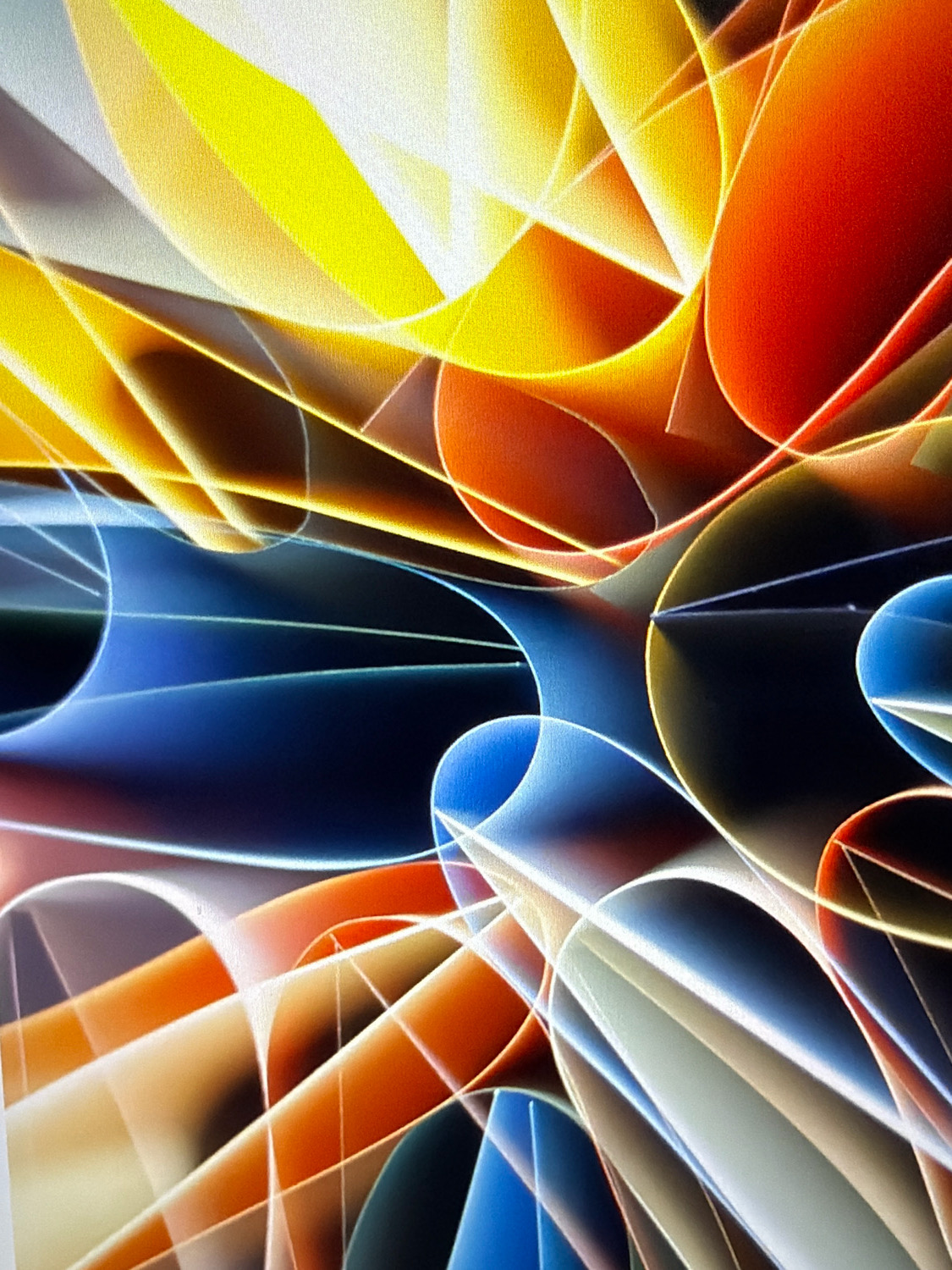 This is an abstract image that appears to be a close-up of colorful, curved shapes. There are no discernible elements that would place it in a specific city or location. The image consists of flowing lines and planes in vibrant colors such as yellow, orange, red, blue, and white. The lighting creates a sense of depth and highlights the textures, which appear somewhat grainy, possibly due to the photographic process or the surface of the materials used. The composition is dynamic, with the curves intersecting and overlapping, creating a complex and visually engaging pattern. There are no people, objects, actions, interactions, or environmental details that suggest a real-world scene.