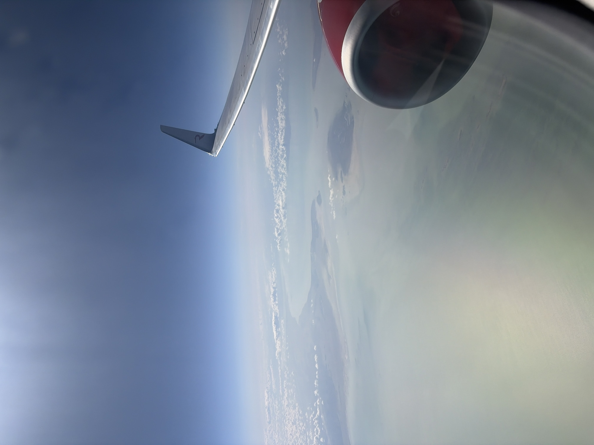 The image shows an airplane wing and engine in flight, with a view of the earth below. The terrain appears to be a coastal region with islands, possibly near the city of Perm, Russia. The image was likely taken from inside the plane.