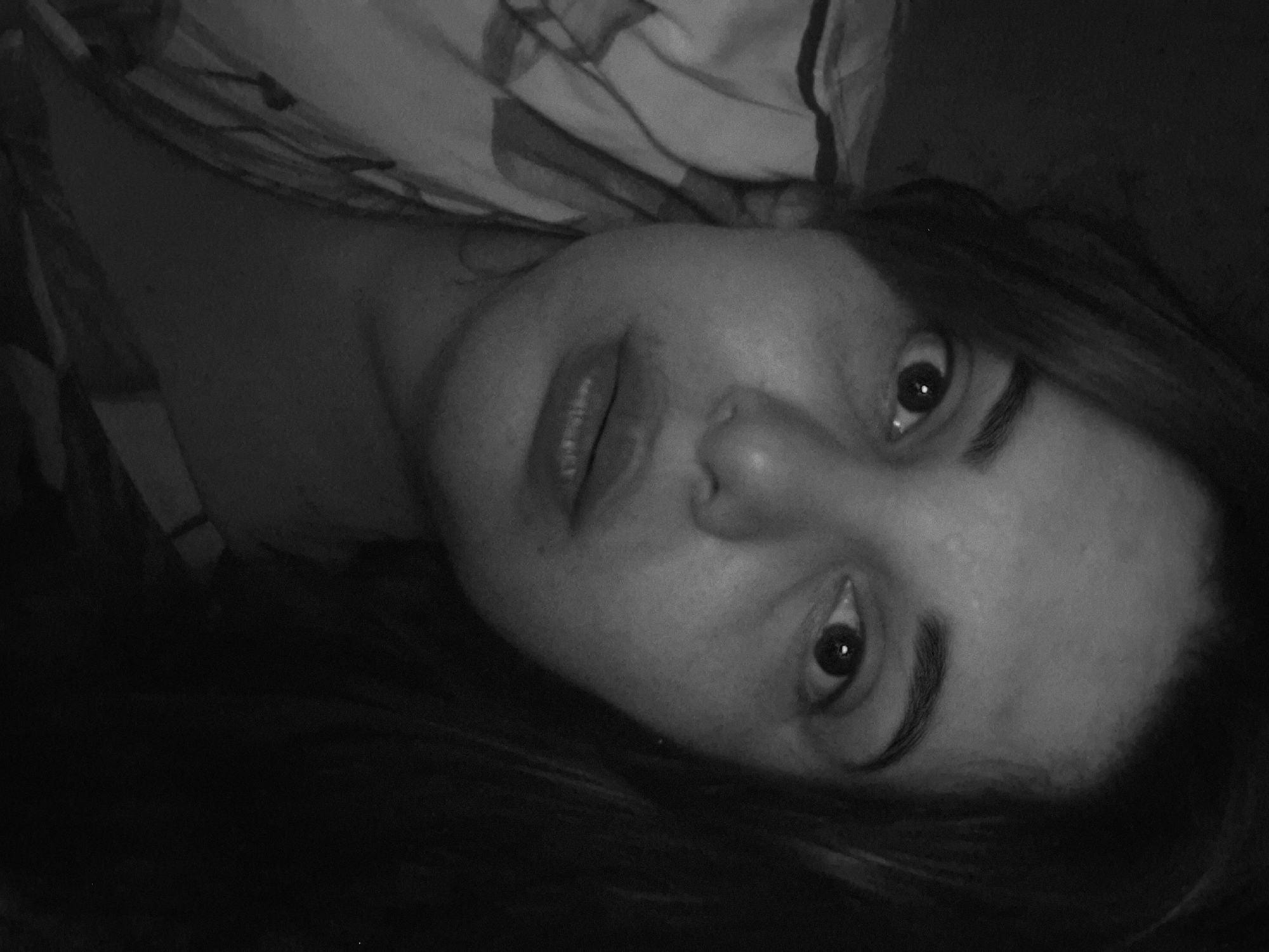 A close-up, black and white photograph shows a woman's face lying at an angle. The woman has medium-length hair. The background consists of what appears to be a patterned bed sheet. The location is not discernible as Амзя, Russia, based on the visual details.