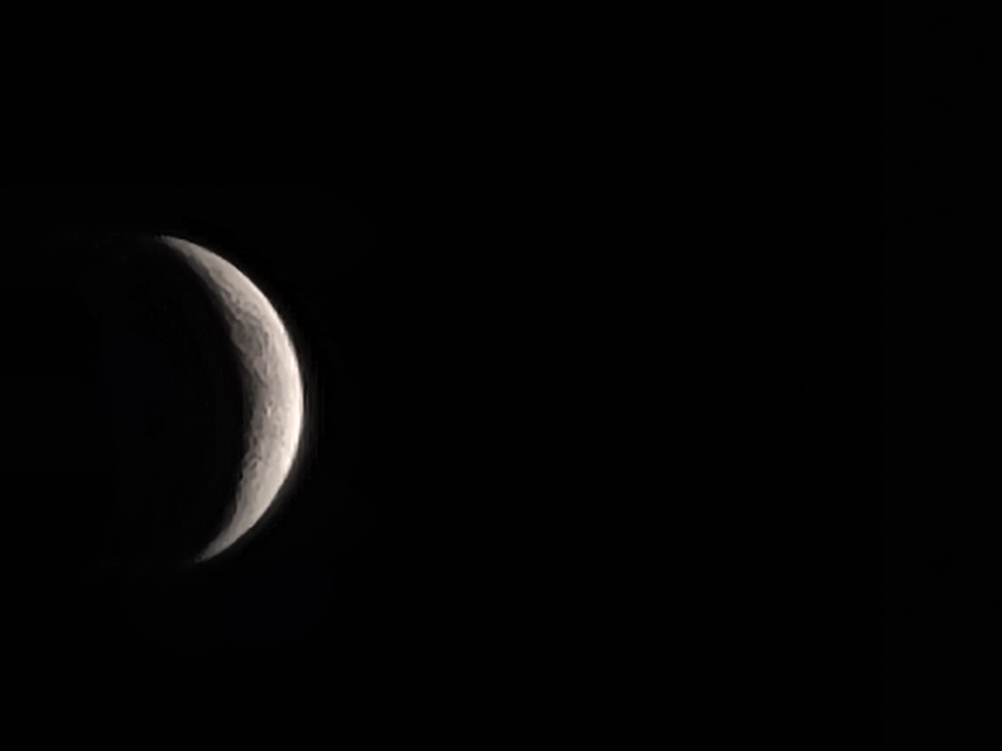 A crescent moon is visible in the dark night sky above Gura Top, Nigeria. The moon is illuminated on its right side, forming a thin arc against the blackness. The rest of the sky is completely dark, suggesting that the image was taken at night. There are no visible man-made structures or natural elements other than the moon and sky.