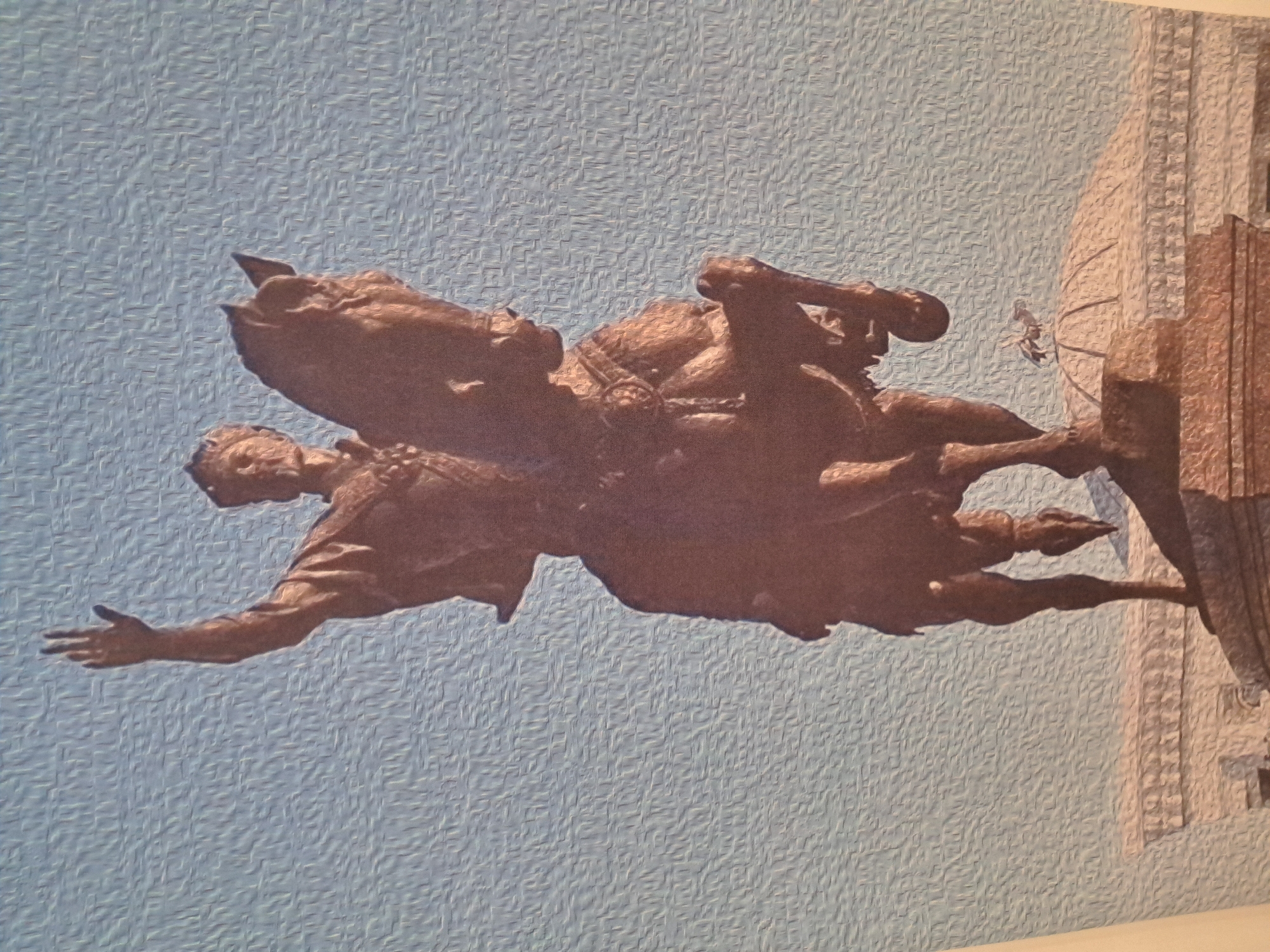 A bronze equestrian statue stands against a textured light blue sky. The statue depicts a man in regal attire, wearing a crown and ornate clothing, with his right arm raised and hand open in a gesture of greeting or command. He is seated on a horse that is rearing upwards on its hind legs. The horse wears a saddle and decorative trappings. Below the statue, a domed structure with intricate architectural detailing is visible, topped by a small, bird-like sculpture. The base of the statue appears to be made of stone. The image has an oil painting effect, with visible brushstrokes throughout. The location is not identifiable from the image itself.