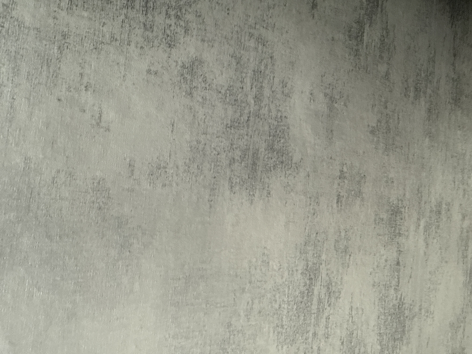 The image shows a close-up of a weathered, textured surface. The color palette consists of variations of gray, from light to dark. The texture appears to be layered, with areas of apparent abrasion or wear revealing darker tones beneath lighter ones. The overall effect resembles a distressed or aged finish, potentially on a wall or similar surface. No people, subjects, objects, actions, or interactions are visible. There is no evidence to determine a location or city.