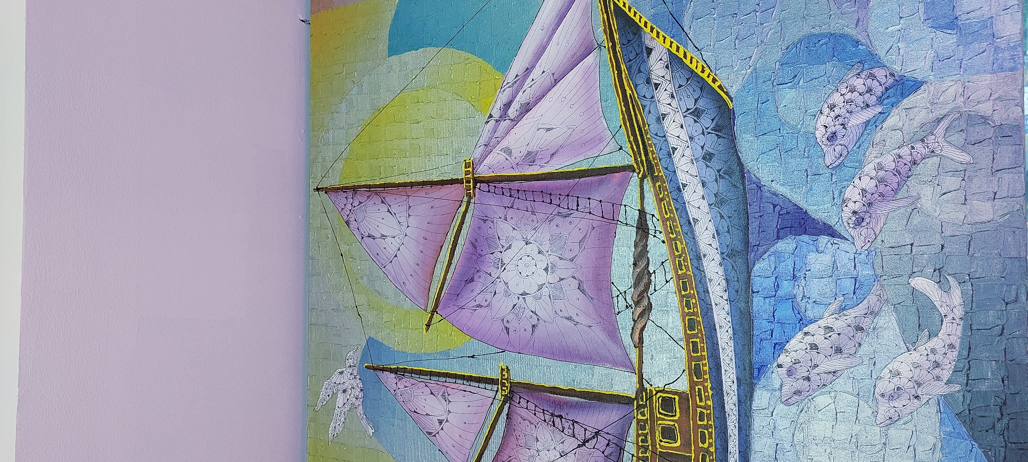 This image depicts a painting on a textured wall, possibly a mural or artwork displayed in a room. The artwork features a sailing ship with purple sails adorned with intricate mandala-like patterns. The ship is depicted at sea, with stylized blue waves and several fish swimming below. In the background, a yellow sun is visible behind a bird in flight. The top portion of the image shows a plain, pale purple wall, likely the surface on which the artwork is mounted. There are no people or specific city elements identifiable within the image itself that would indicate a location in Curug Sangereng, Indonesia. The scene is entirely artistic and fantastical.