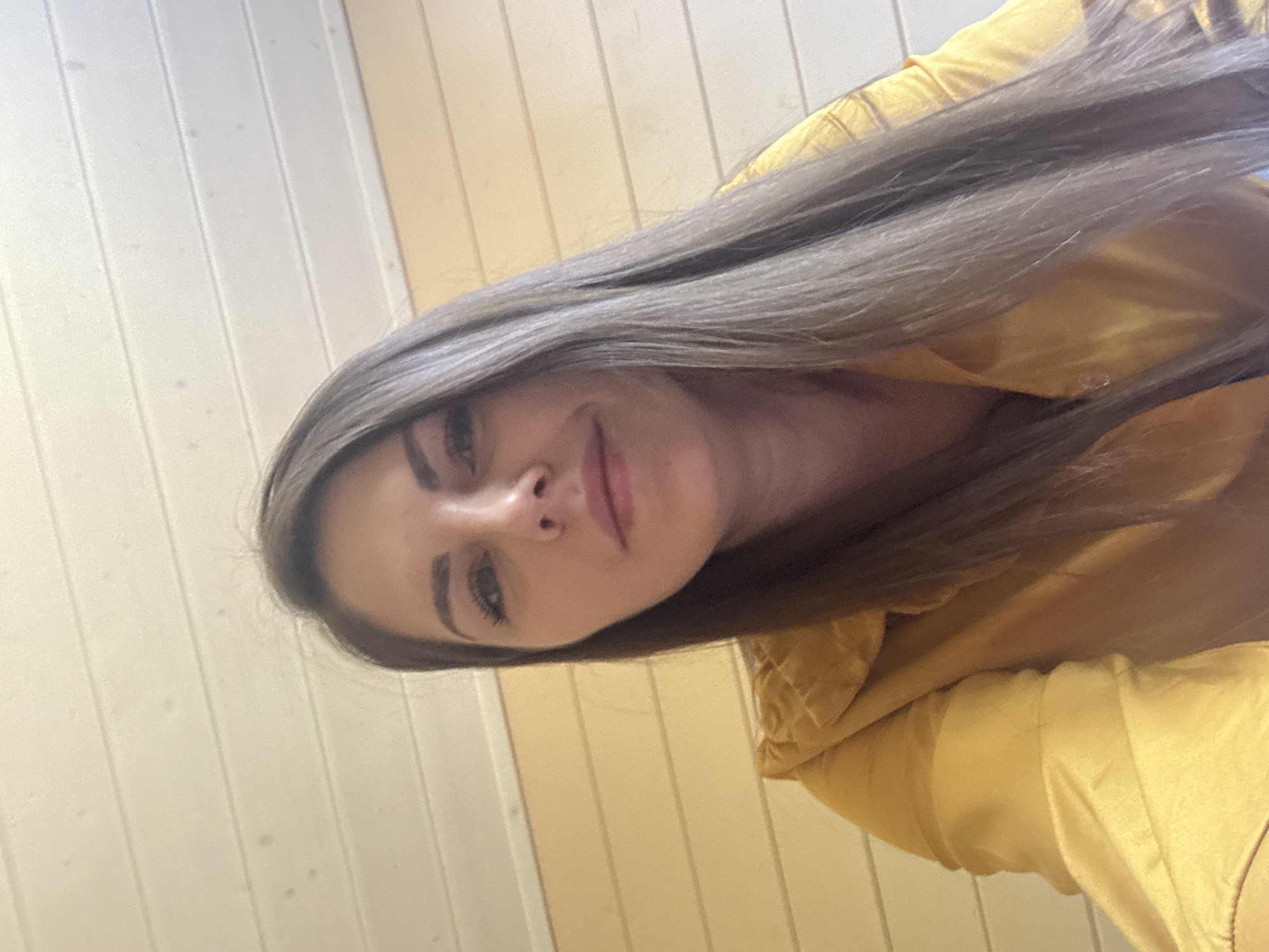 A woman with long, light brown hair, wearing a yellow top, is pictured indoors. The background consists of light-colored vertical panels. The image was presumably taken in Раздолье, Russia.
