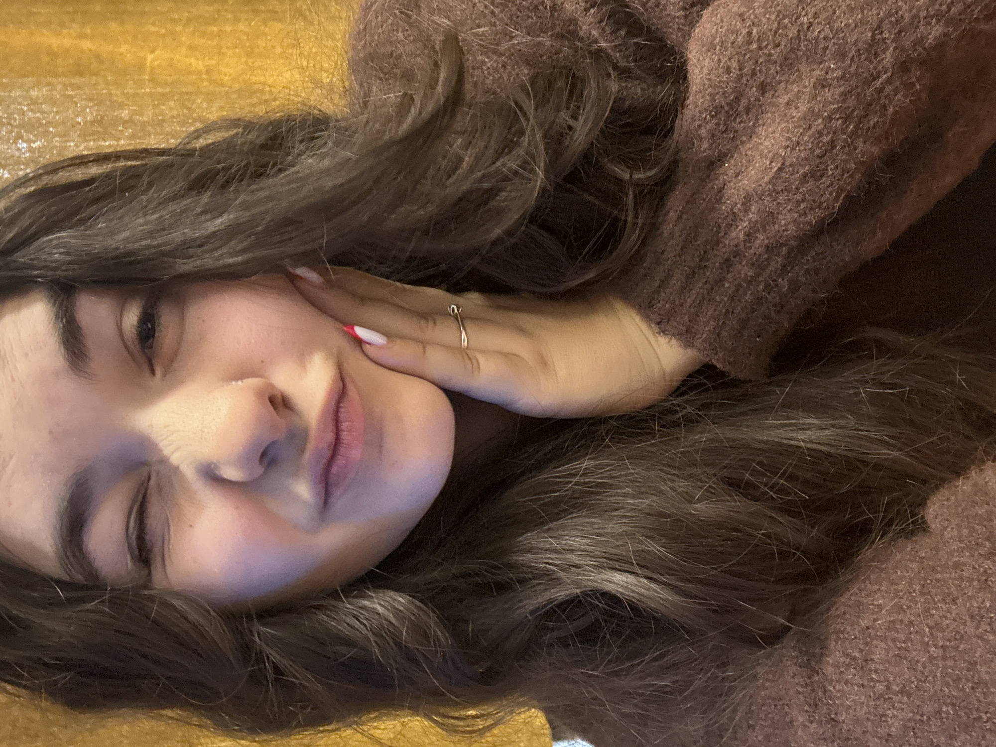 A young woman is lying on a wooden surface, resting her head on her hand. She is wearing a brown sweater. She is indoors. There is no indication of the location being Plovdiv, Bulgaria, or any specific city.